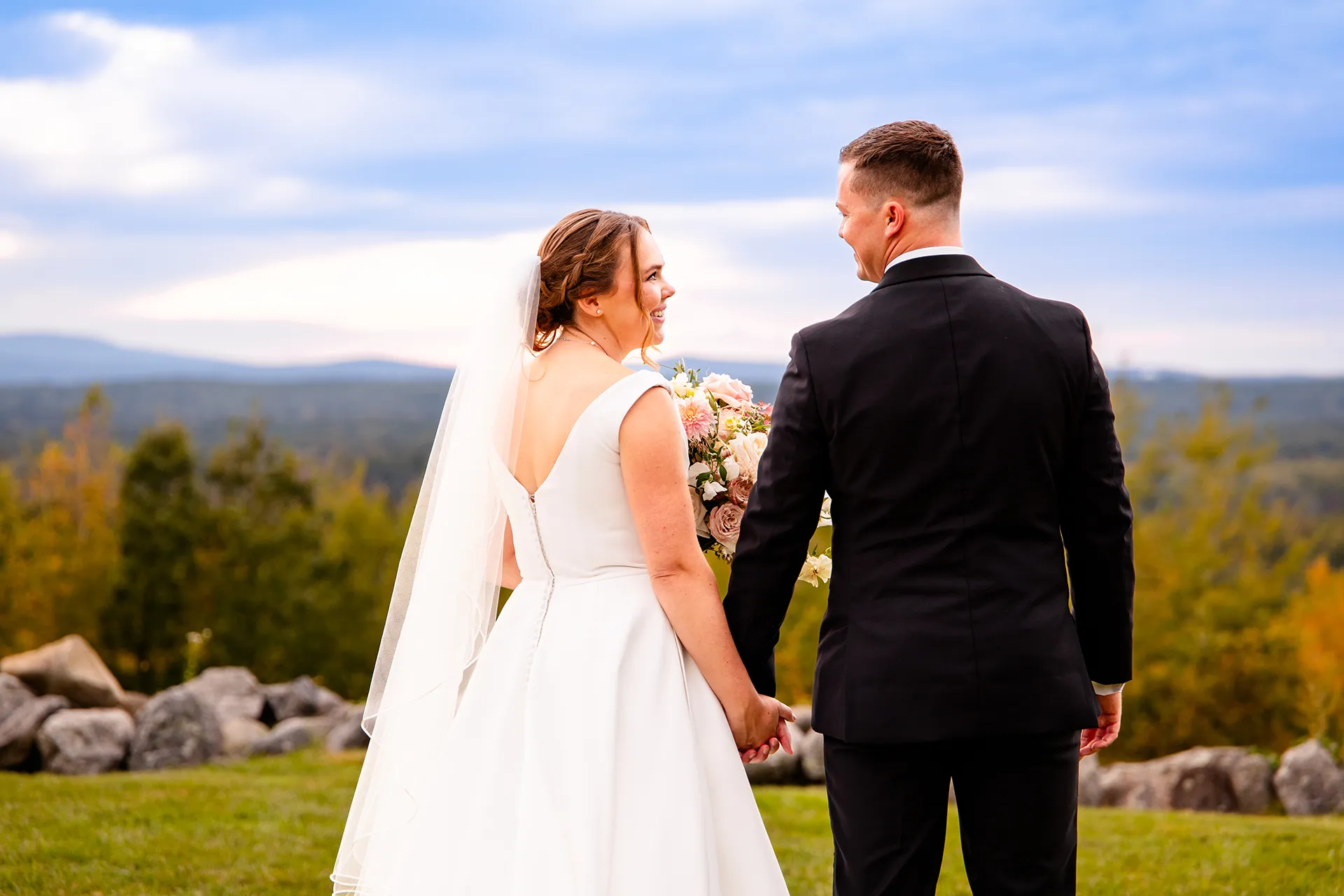 A bride holds a groom's hand and smiles at him during wedding portraits at Fruitlands Museum in Harvard, Massachusetts.