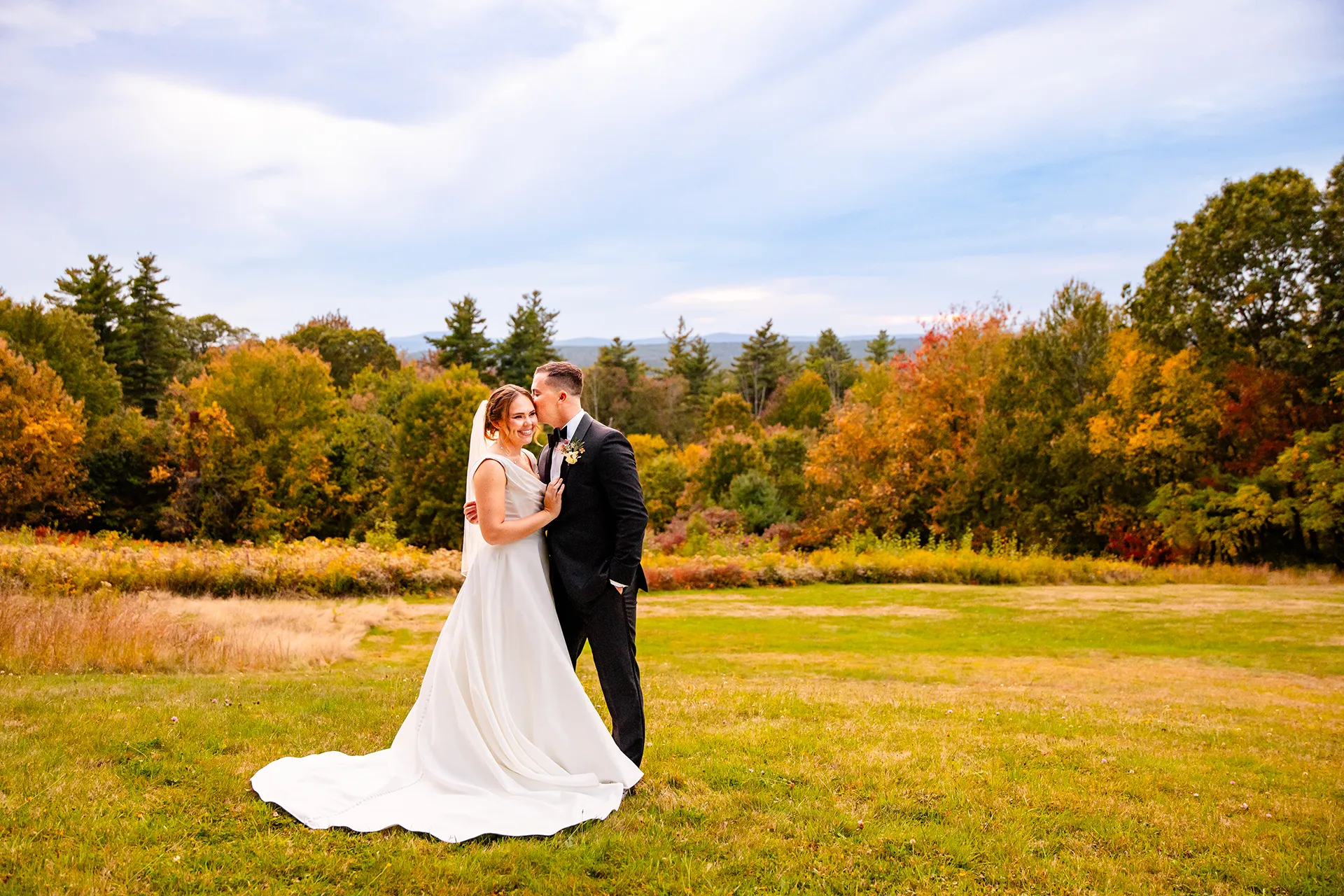 A groom kisses a smiling bride during fall wedding portraits at Fruitlands Museum in Harvard, Massachusetts.