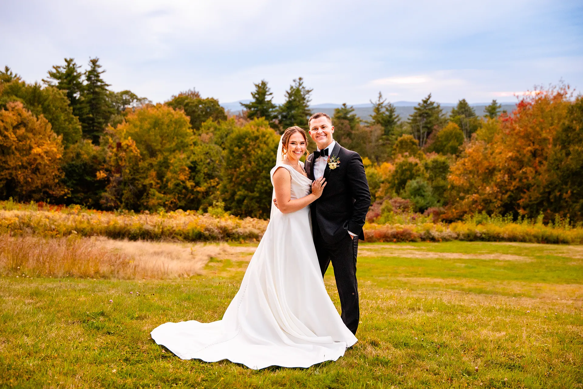 A bride and groom smile and pose during fall wedding portraits at Fruitlands Museum in Harvard, Massachusetts.