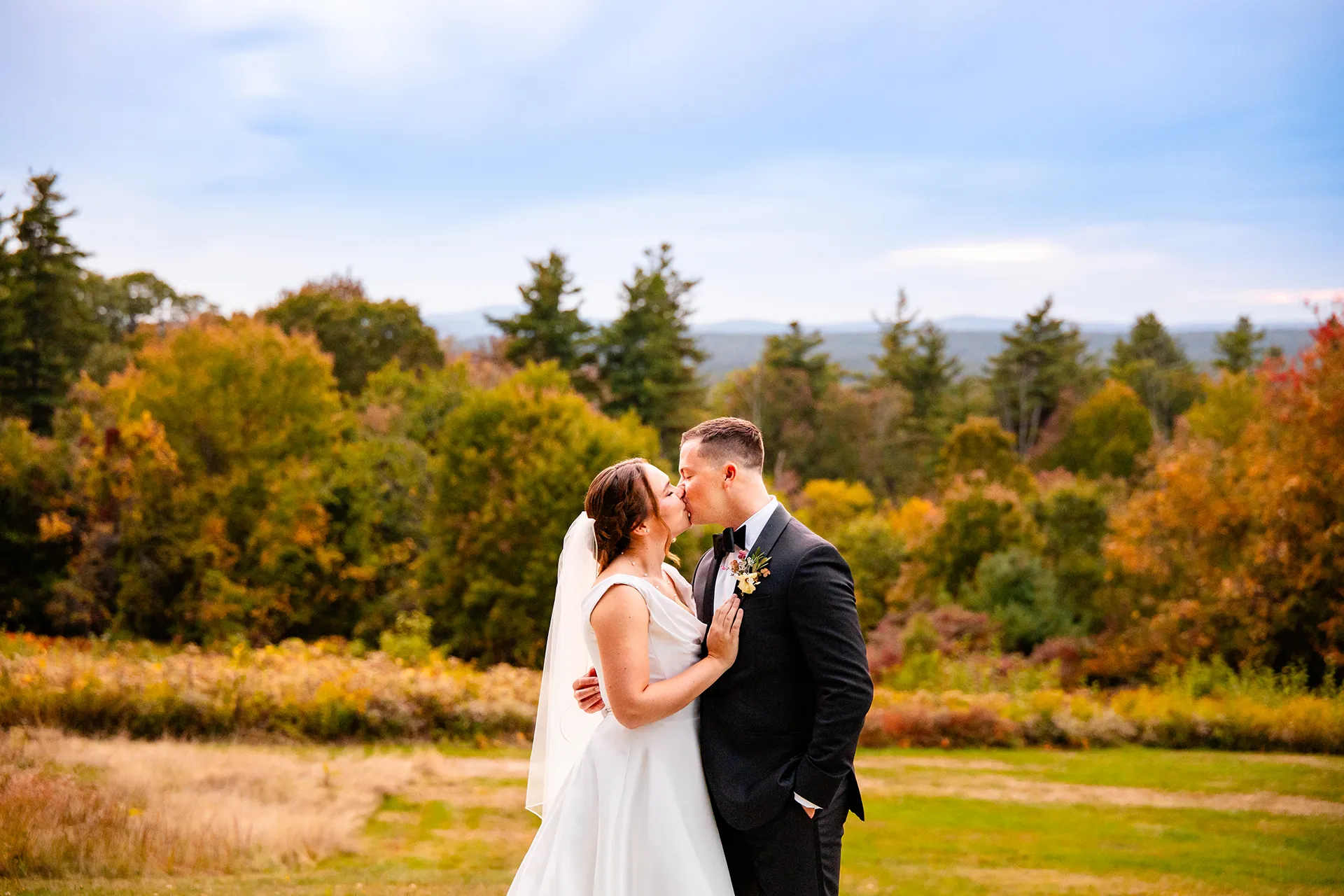 A bride and groom kiss in front of fall foliage during wedding portraits at Fruitlands Museum in Harvard, Massachusetts.