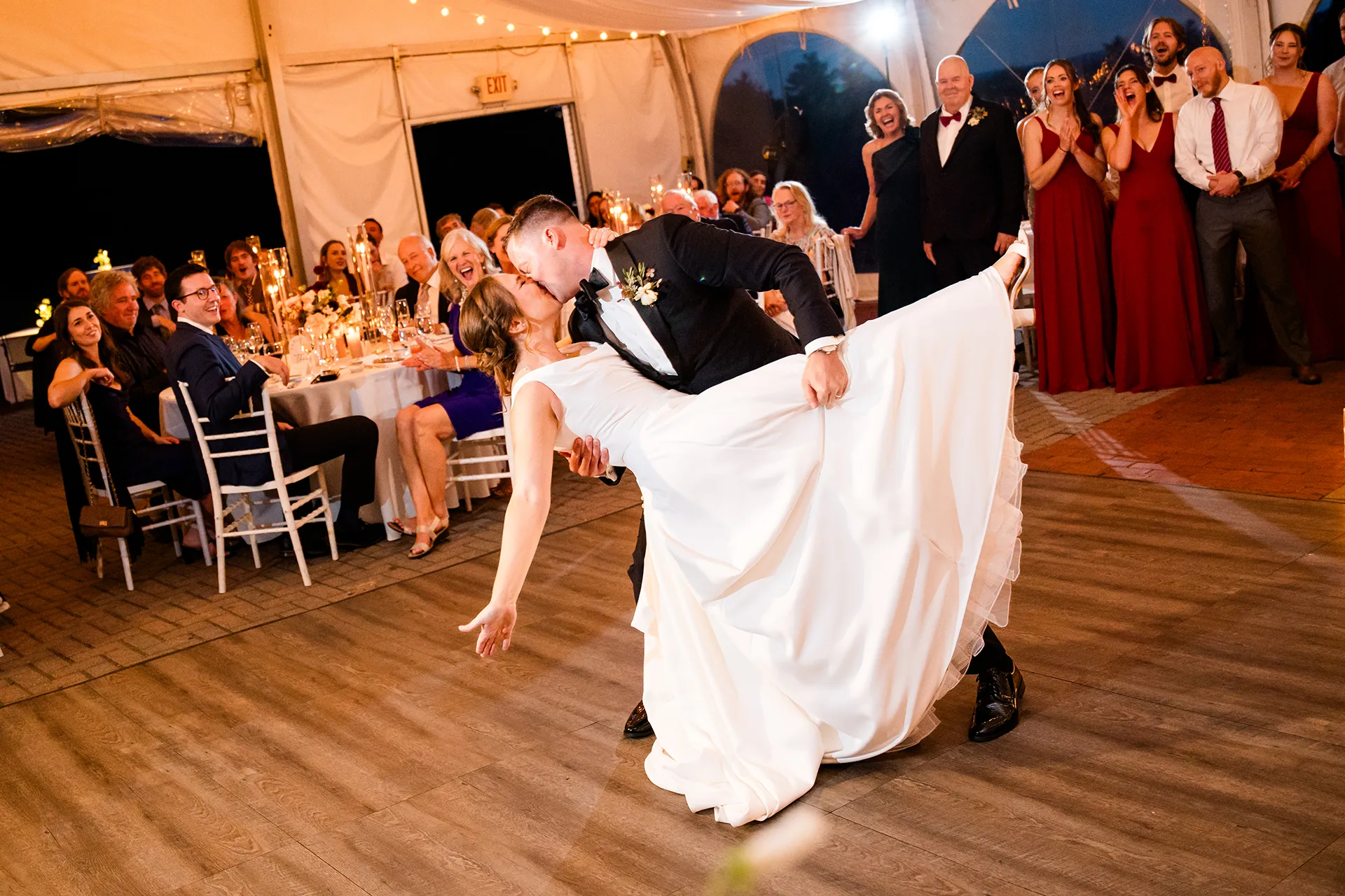 A groom dips a bride as they kiss and guests cheer during a wedding reception at Fruitlands Museum in Harvard, Massachusetts.