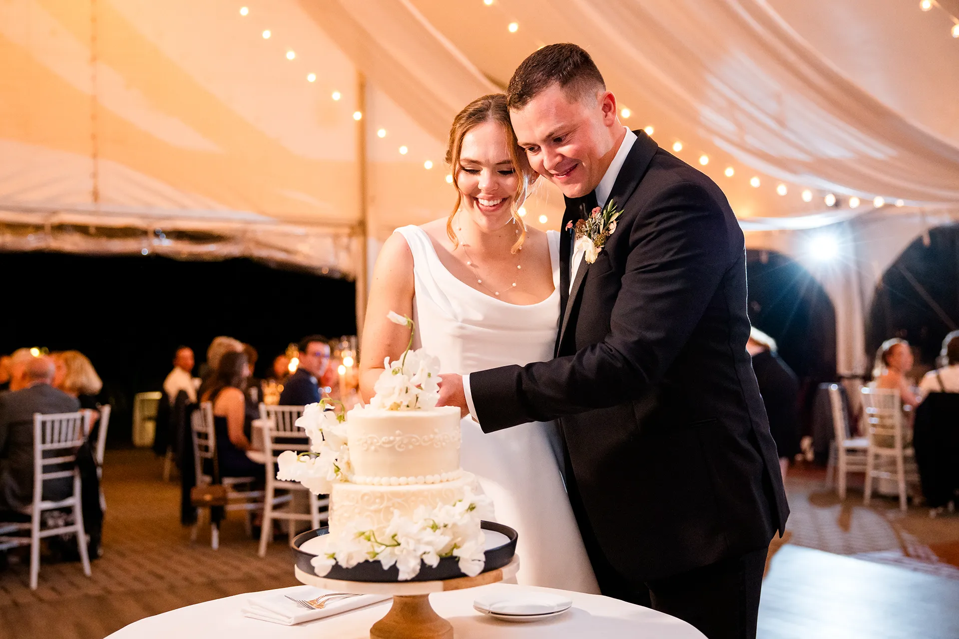A bride and groom cut a white wedding cake during a reception at Fruitlands Museum in Harvard, Massachusetts.