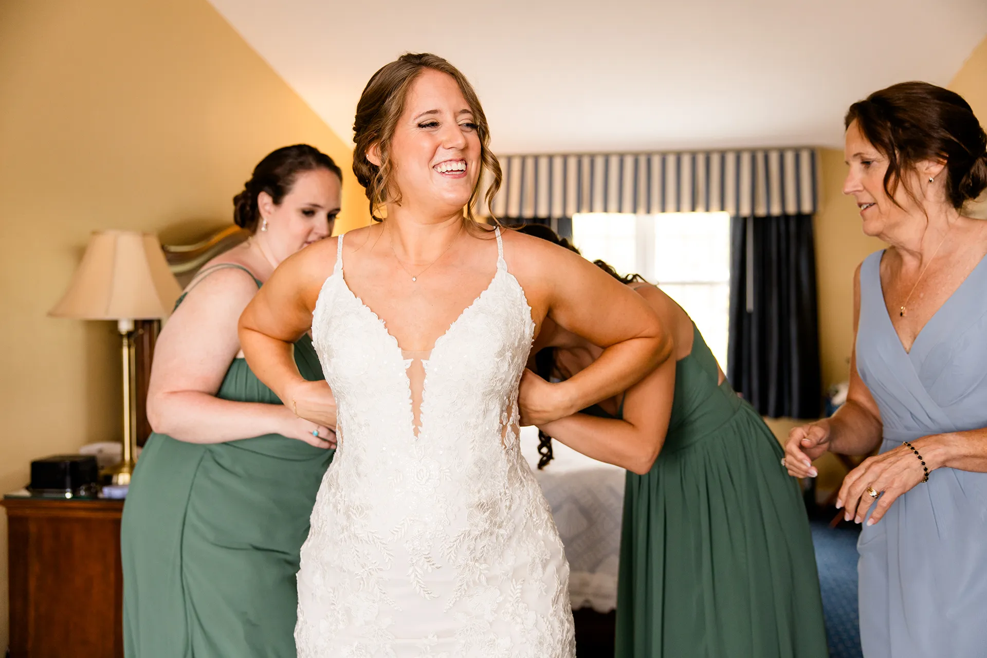 maine wedding photography meghan phil 12 A bride smiles as she is helped in her dress by her bridesmaids at the Atlantic Oceanside Hotel and Event Center in Bar Harbor, Maine.