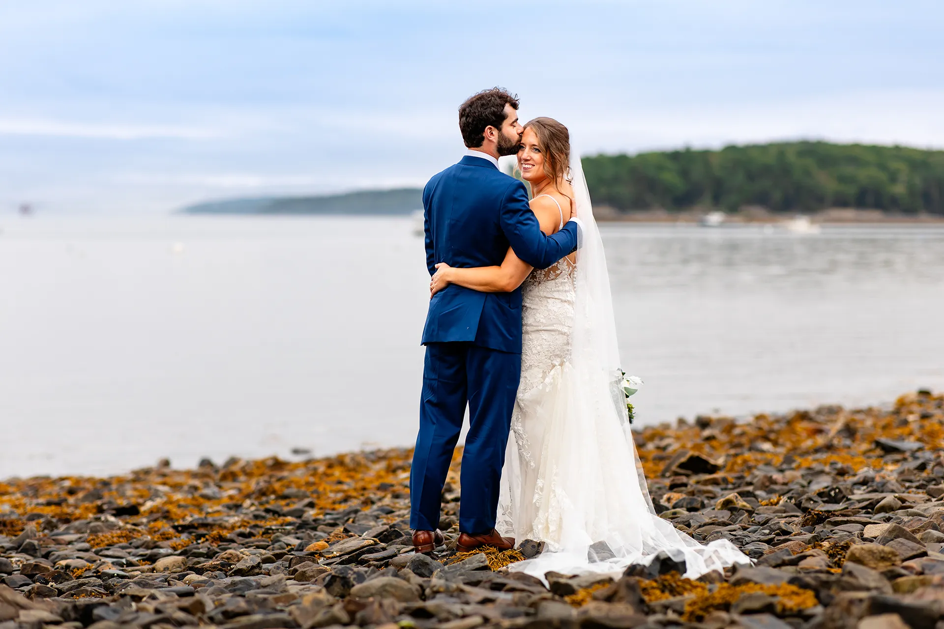 maine wedding photography meghan phil 53 A bride smiles as a groom kisses her on the head during beach wedding portraits at the Atlantic Oceanside Hotel & Event Center in Bar Harbor, Maine.