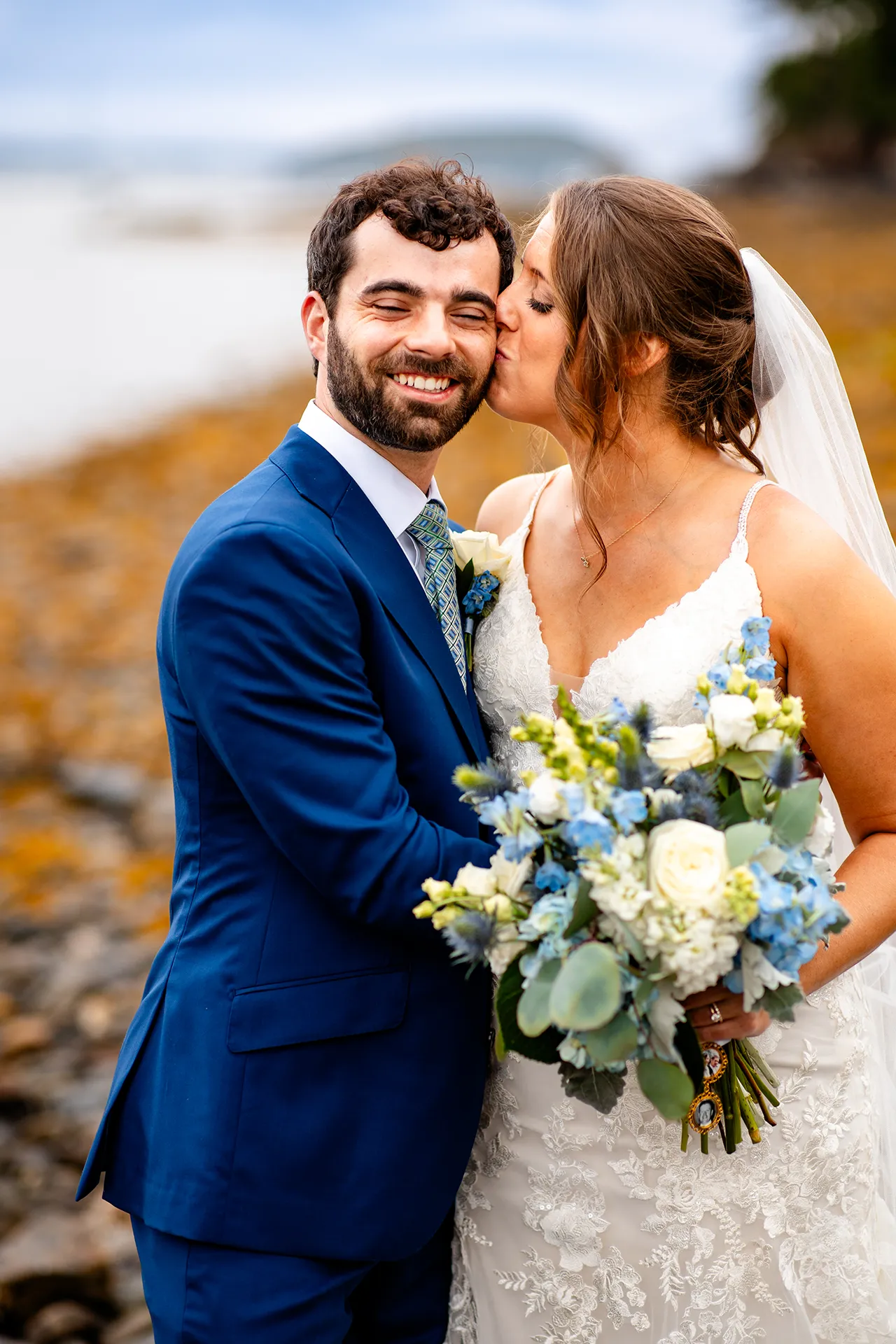 maine wedding photography meghan phil 54 A groom smiles as a bride kisses him on the cheek during beach wedding portraits at the Atlantic Oceanside Hotel & Event Center in Bar Harbor, Maine.