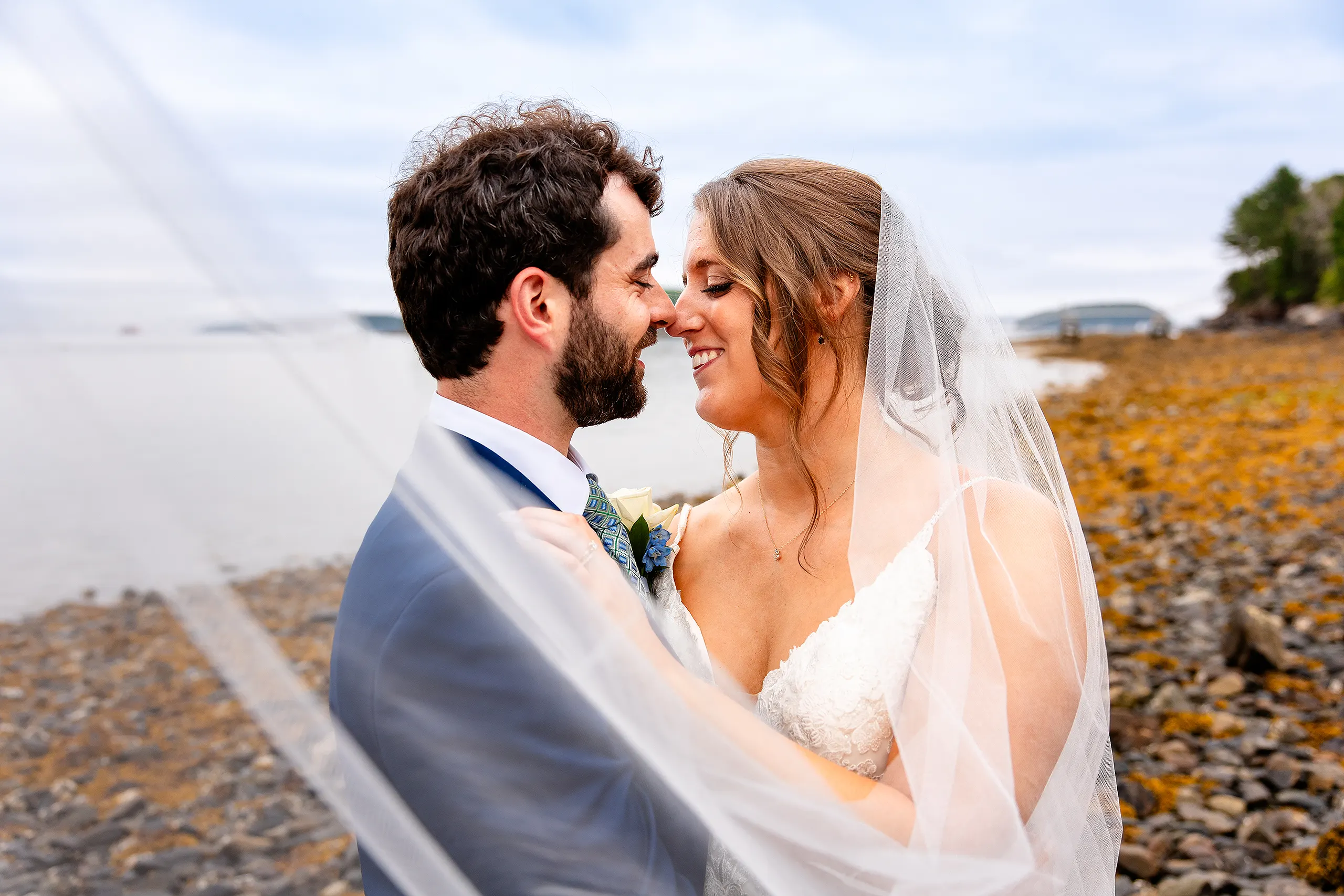 A bride and groom rub noses and smile during beach wedding portraits at the Atlantic Oceanside Hotel & Event Center in Bar Harbor, Maine.