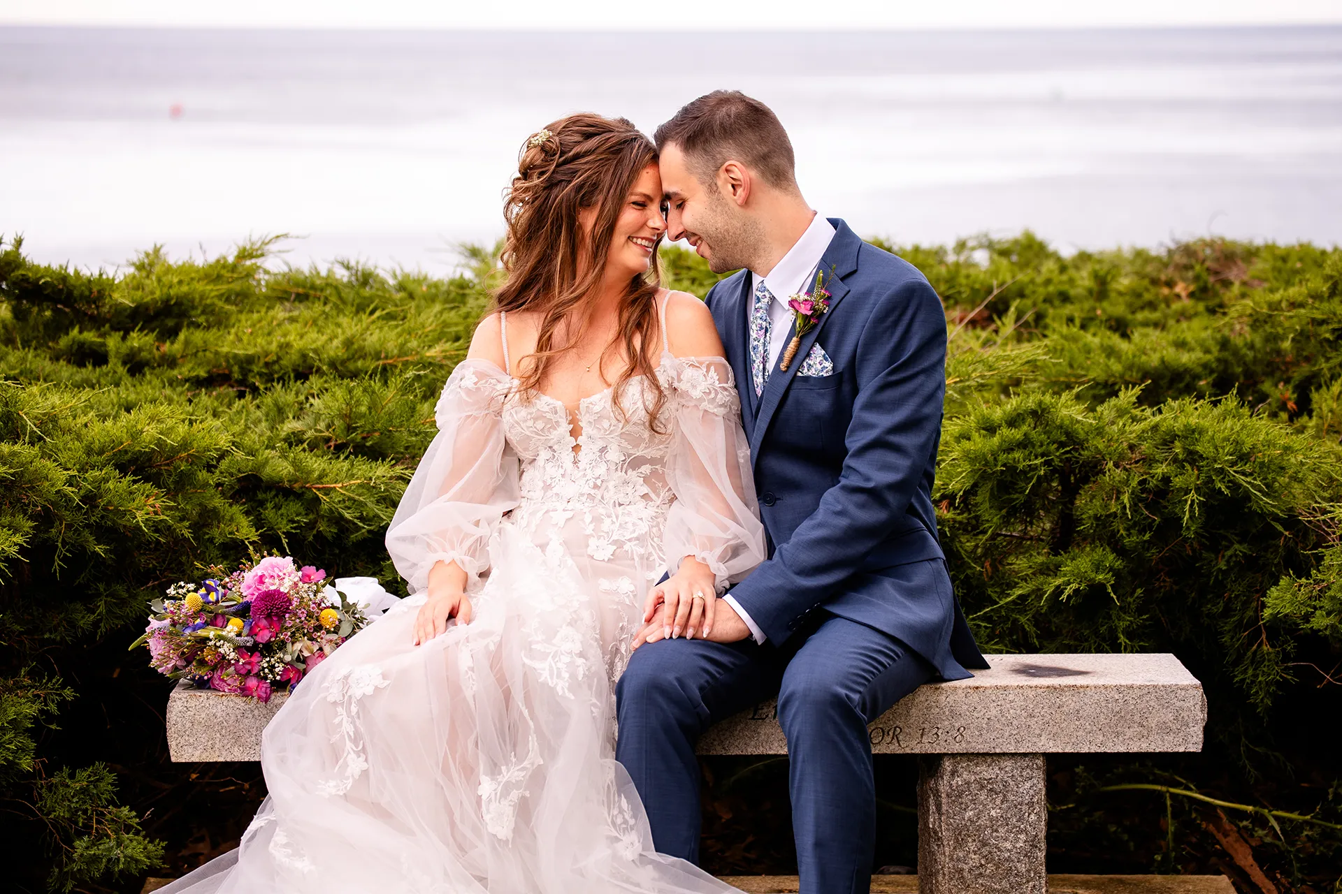 A bride and groom sit and smile at each other during wedding portraits at Hartley Mason Reserve in York, Maine.