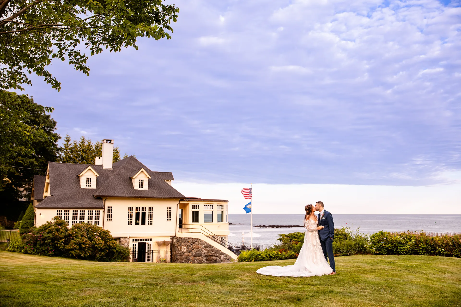 A bride and groom kiss in front of the York Harbor Reading Room during wedding portraits in York, Maine.