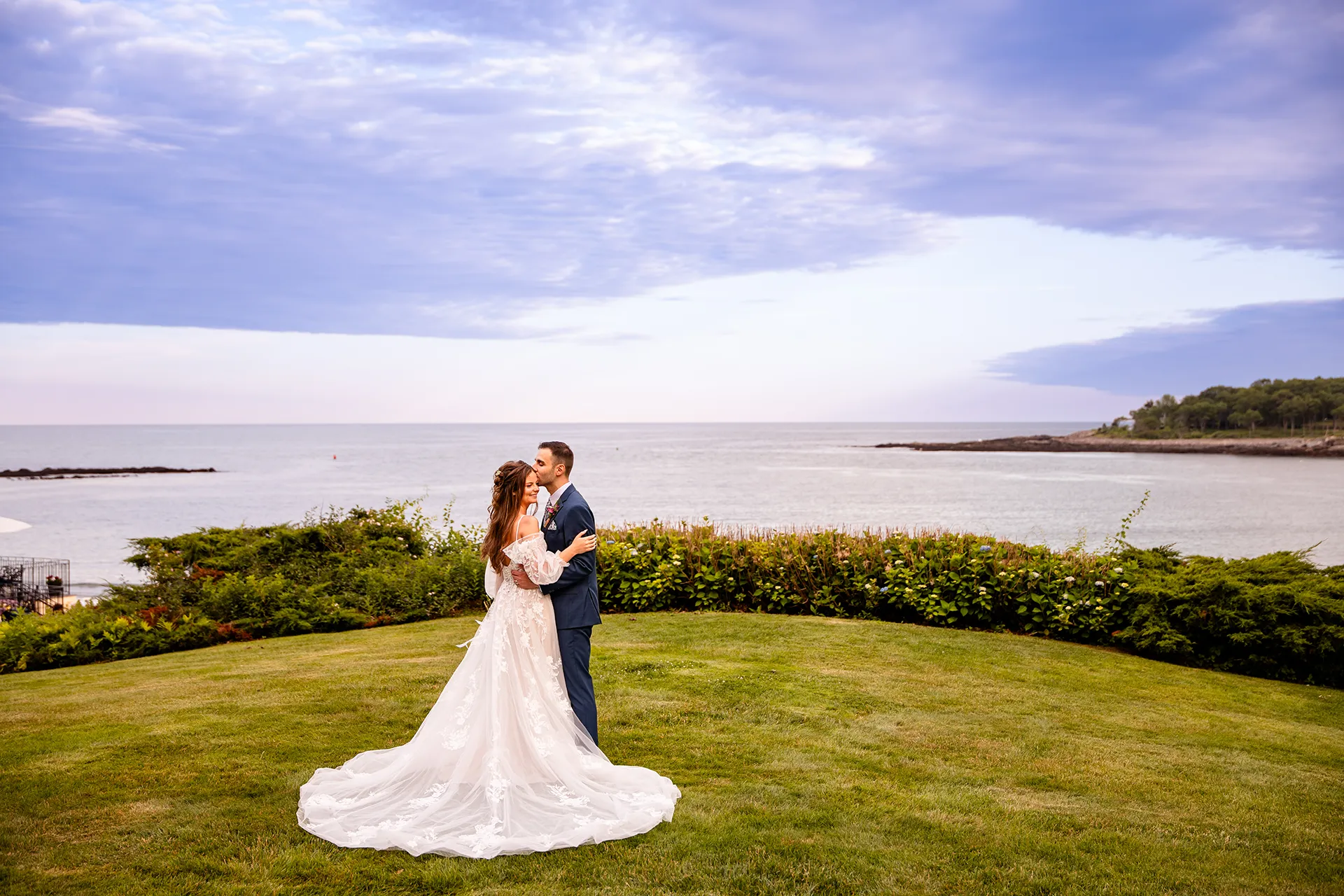 A groom kisses a bride on the head during wedding portraits at the Hartley Mason Reserve near the York Harbor Reading Room in York, Maine.
