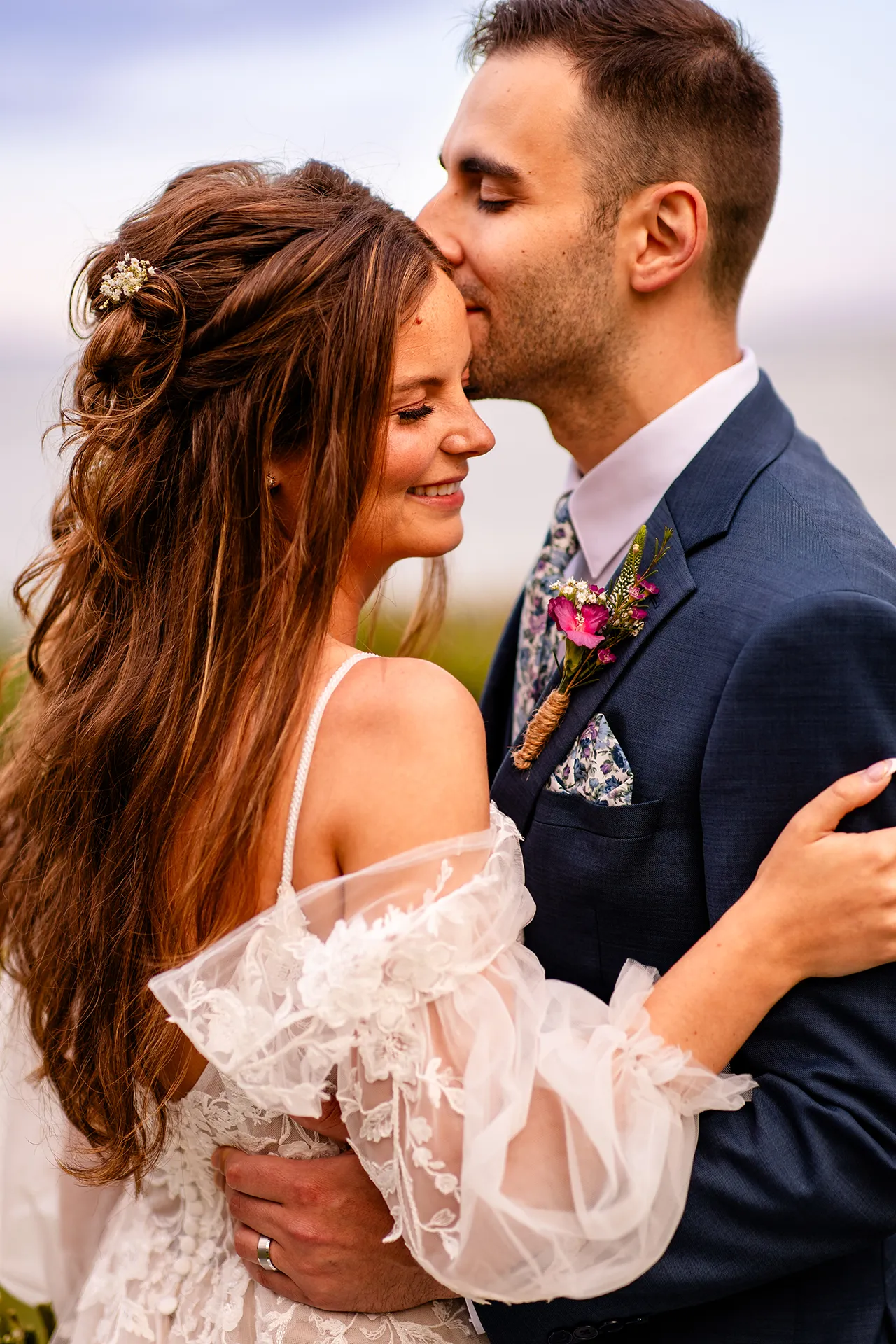 A bride smiles as a groom kisses her on the head during wedding portraits at the Hartley Mason Reserve in York, Maine.