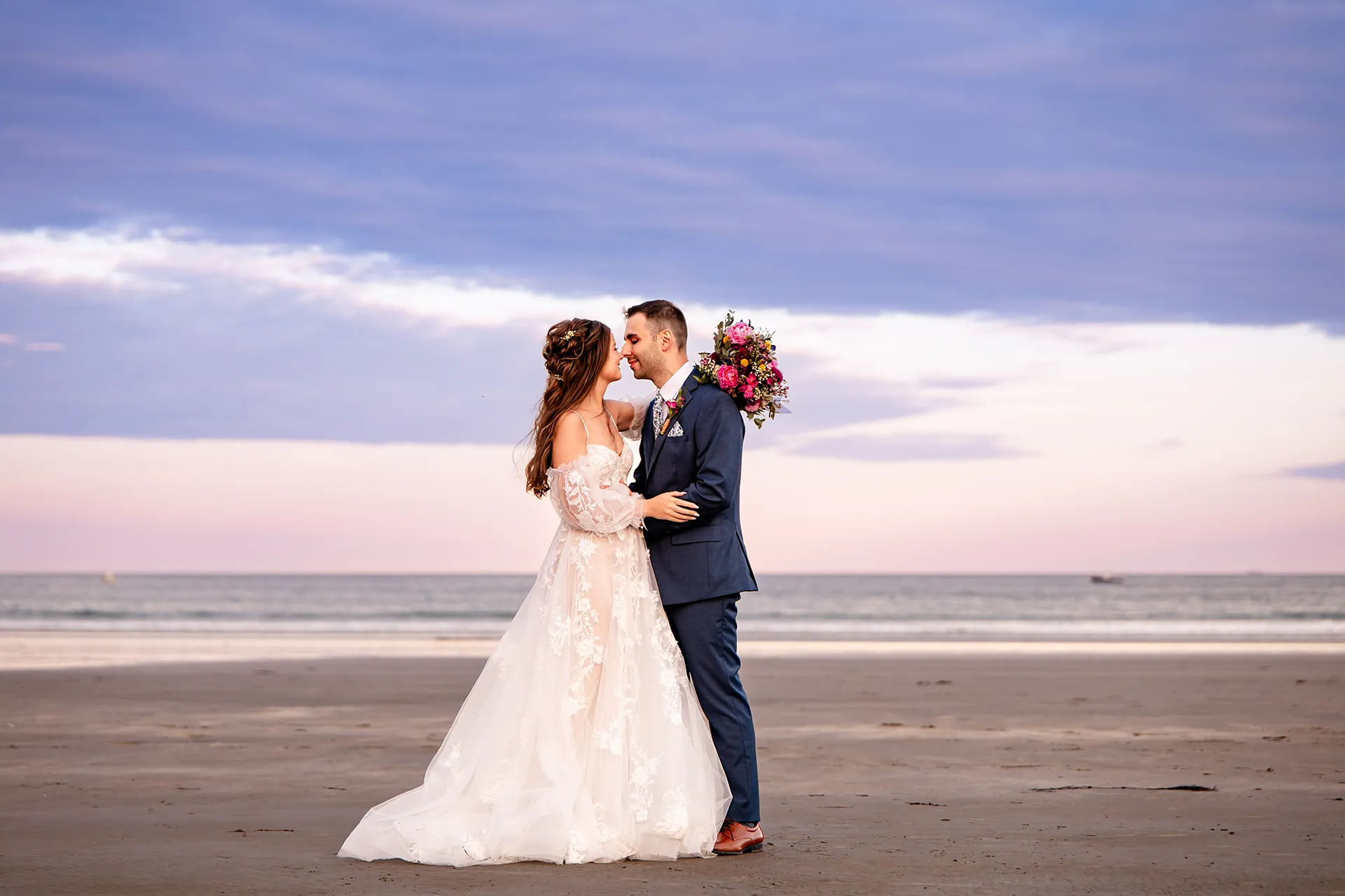 A bride and groom smile as they rub noses during sunset wedding portraits at Long Sands Beach in York, Maine.