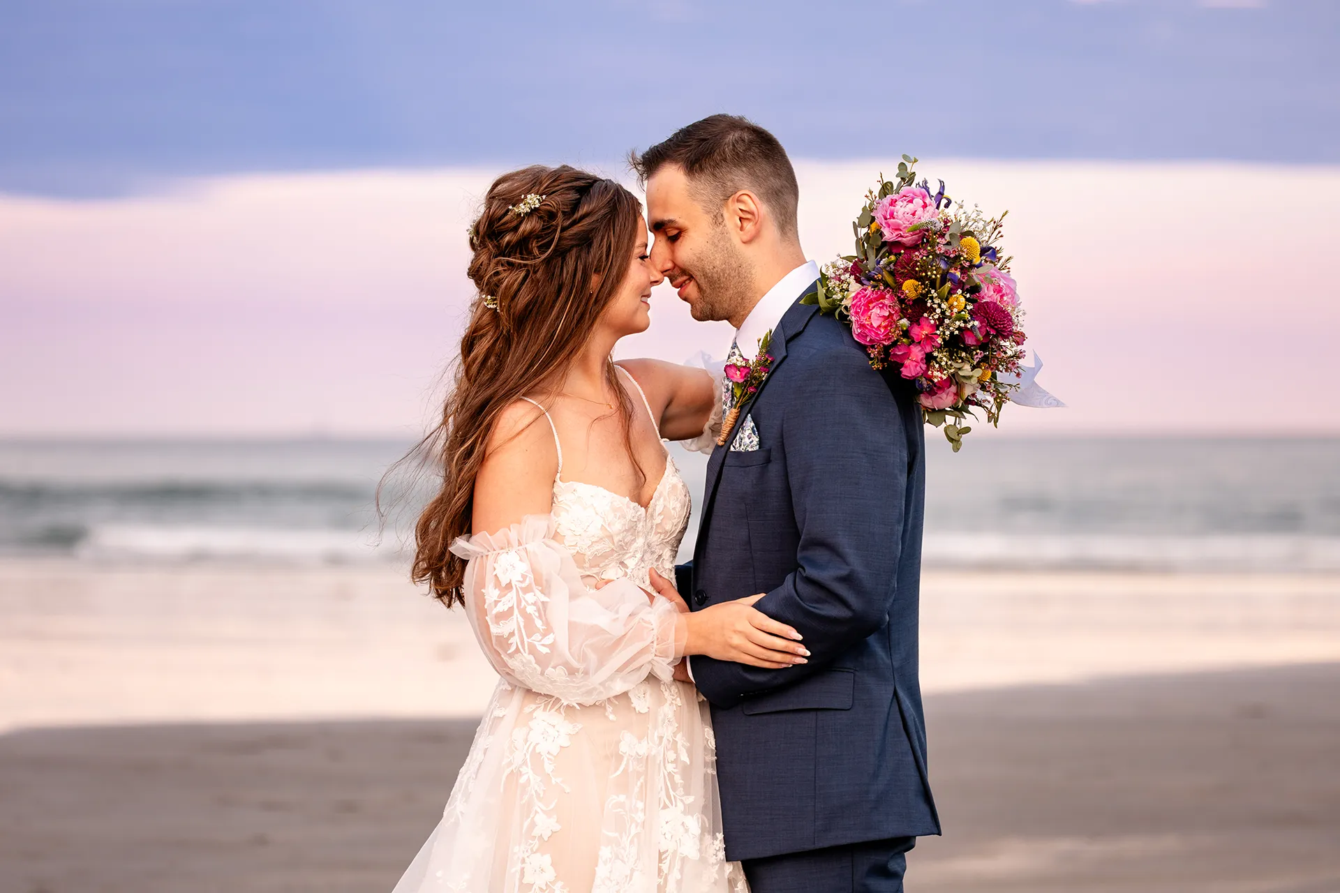 A bride and groom smile as they rest their heads together during sunset wedding portraits at Long Sands Beach in York, Maine.