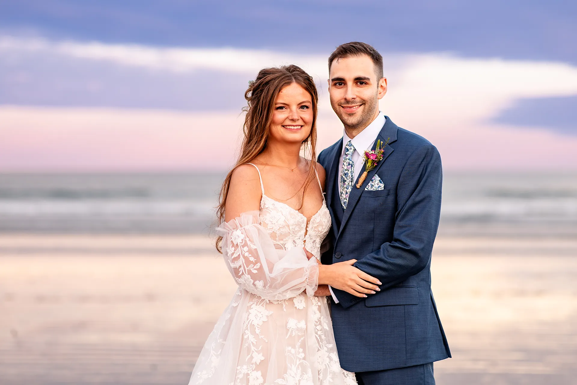 A bride and groom smile and pose during sunset wedding portraits at Long Sands Beach in York, Maine.