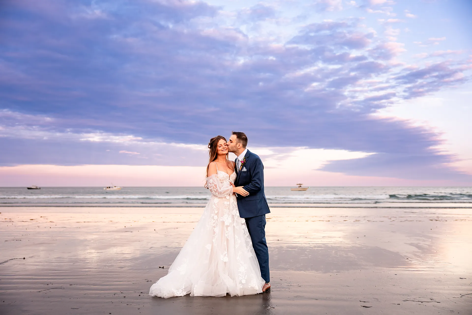 A groom kisses a bride on the cheek as the sunsets during wedding portraits at Long Sands Beach in York, Maine.