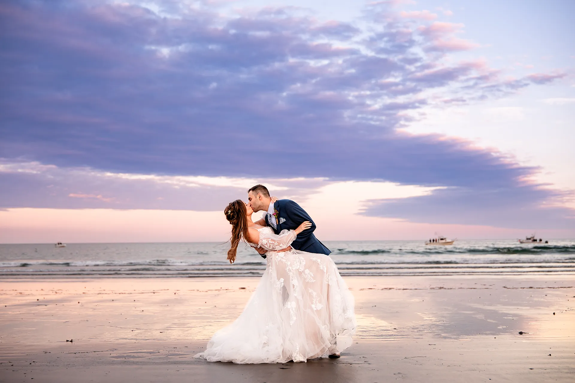 A groom dips a bride as they kiss during sunset wedding portraits at Long Sands Beach in York, Maine.