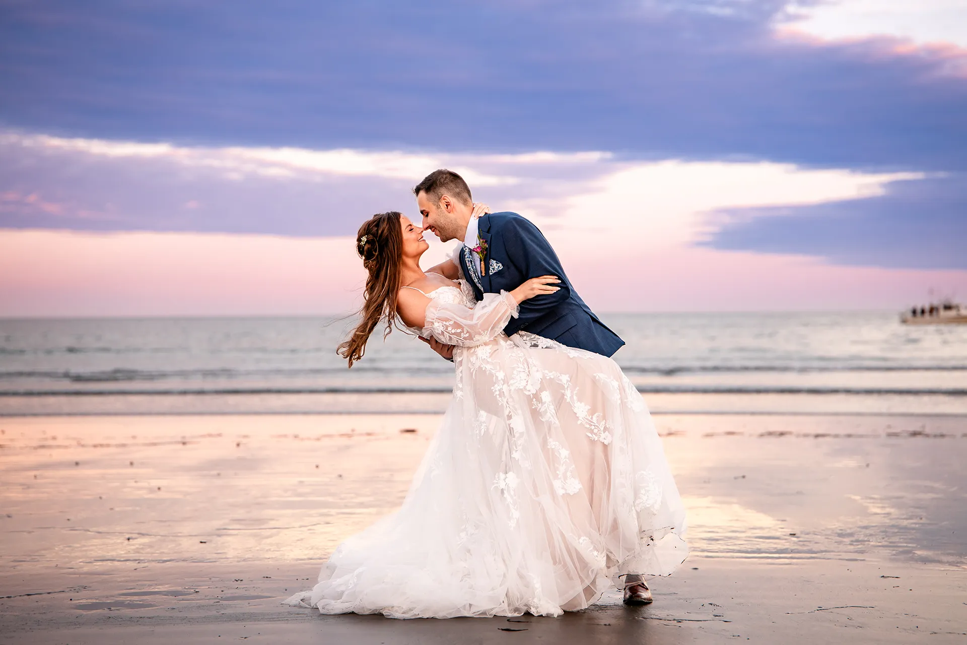 A groom dips a bride as they smile at each other during wedding portraits at Long Sands Beach in York, Maine.