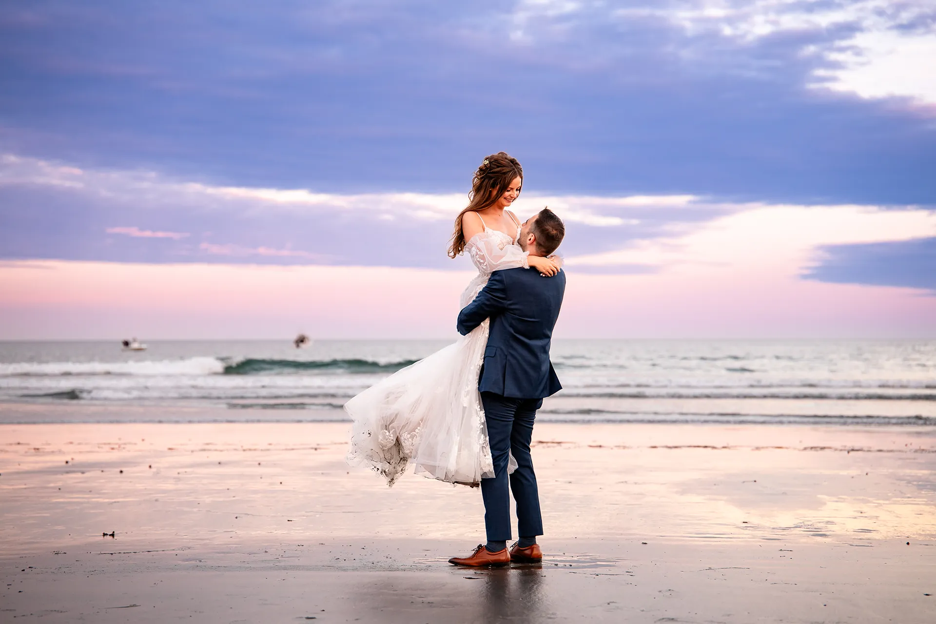 A groom lifts a smiling bride as the sun sets during wedding portraits at Long Sands Beach in York, Maine.