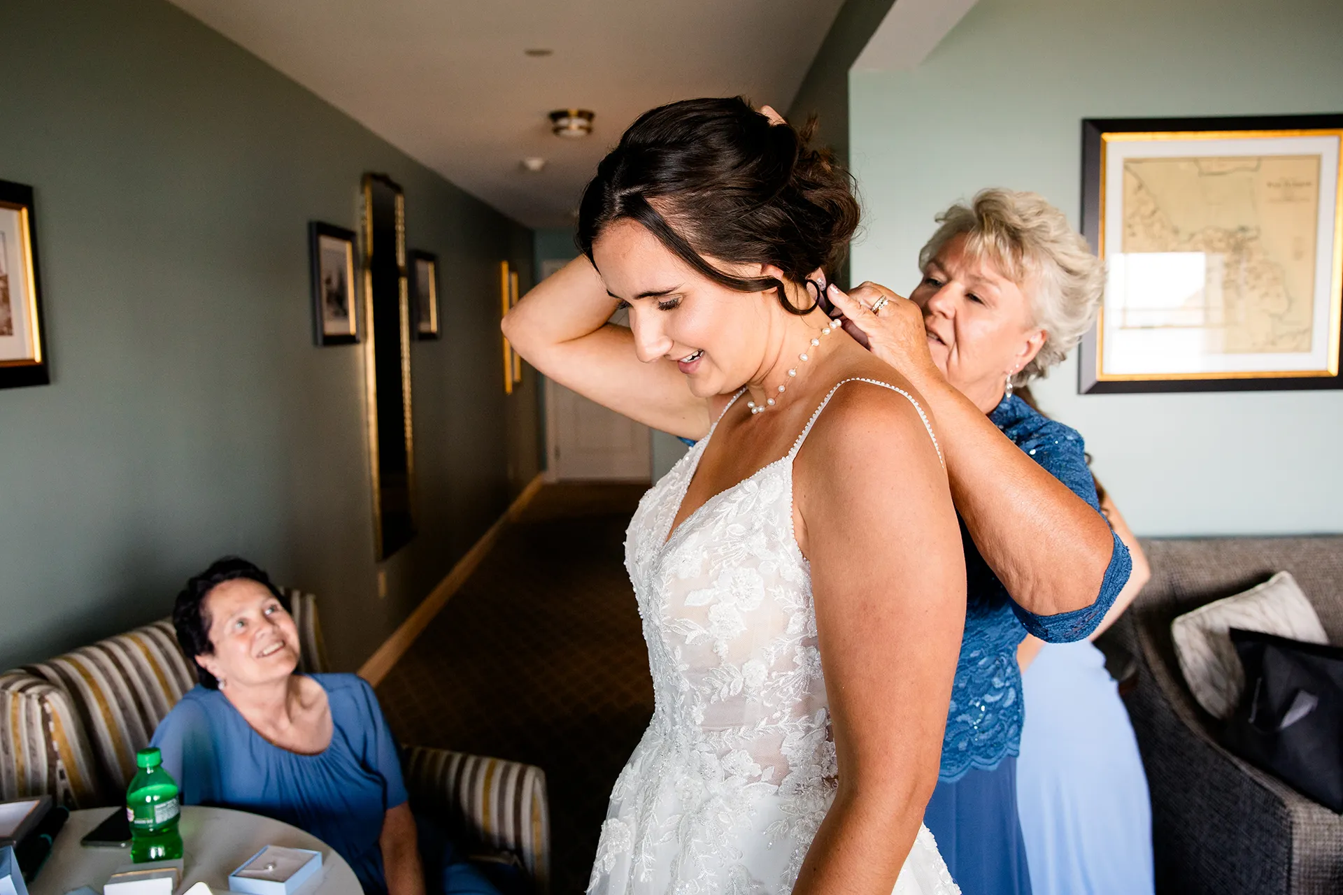 A bride smiles as her mom puts on her necklace as she gets ready for a wedding at the Bar Harbor Inn and Spa in Bar Harbor, Maine.
