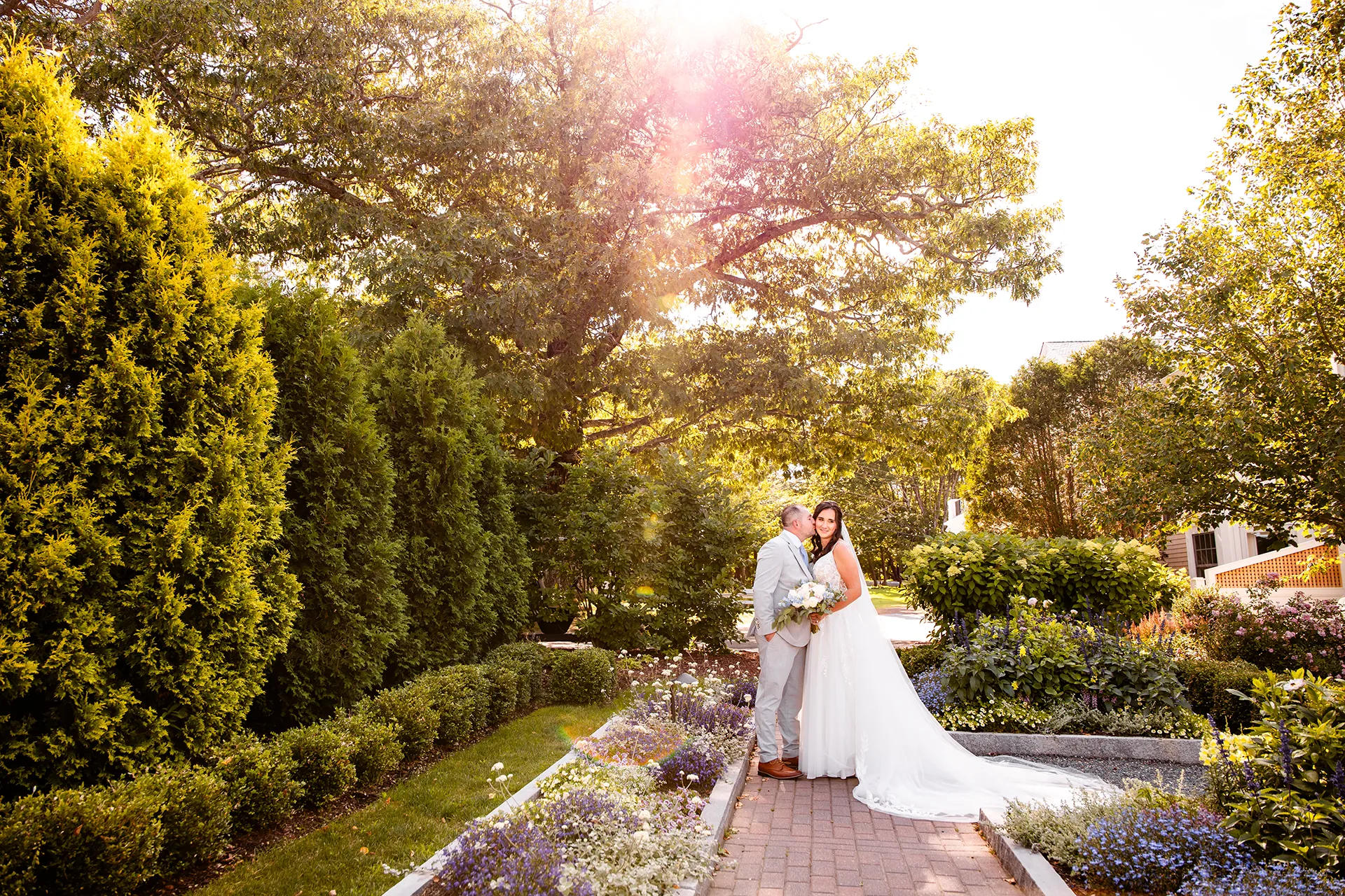 A groom kisses a bride on the cheek while they stand in a garden at the Bar Harbor Inn and Spa in Bar Harbor, Maine.