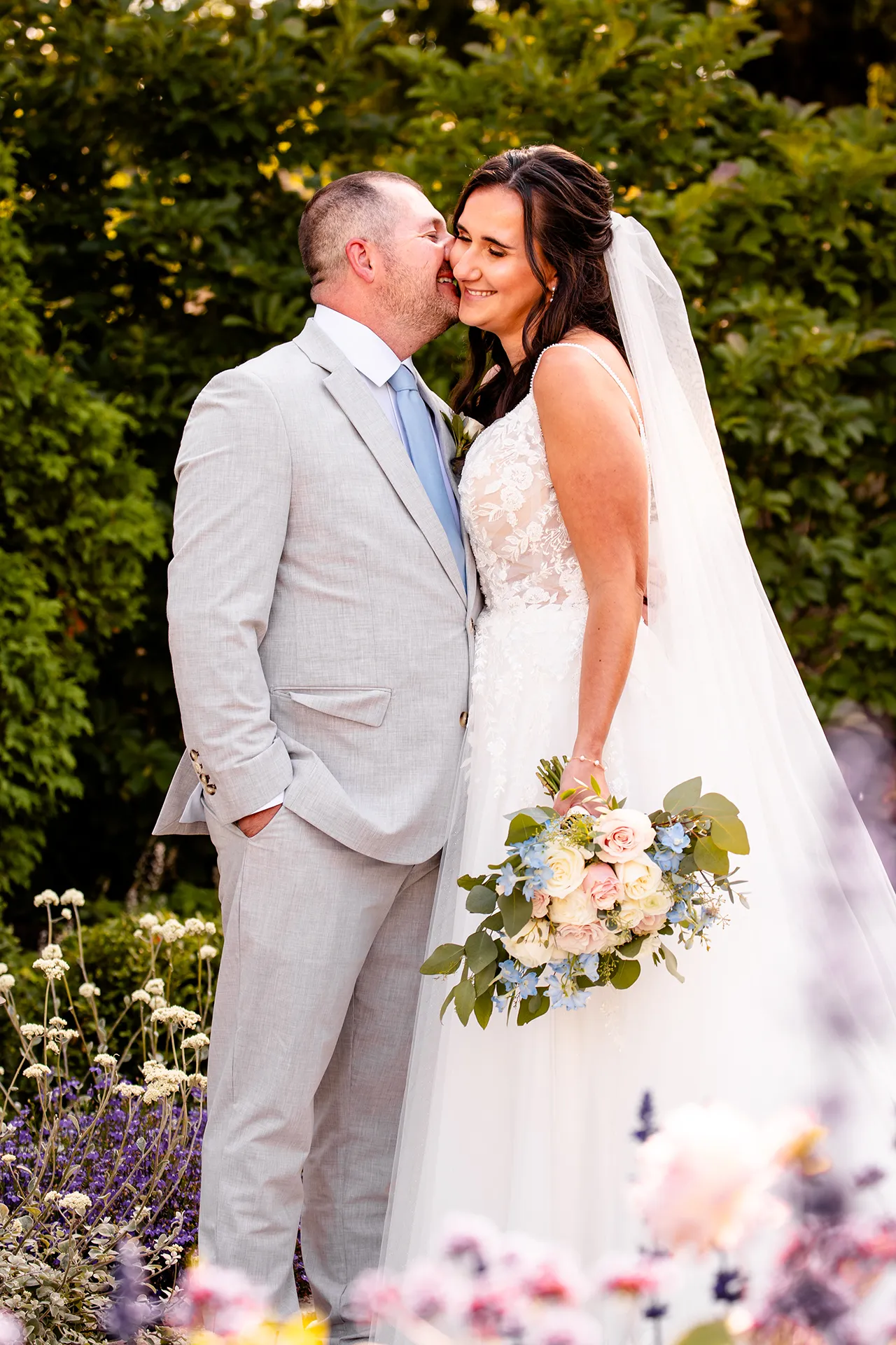 A groom and bride snuggle together in a garden during wedding portraits at the Bar Harbor Inn and Spa in Bar Harbor, Maine.
