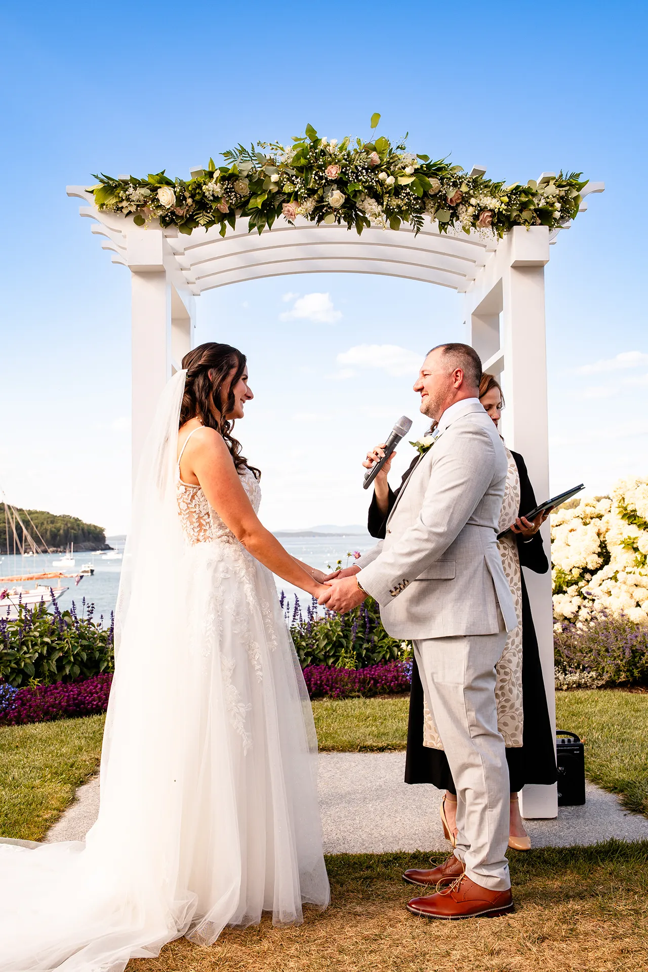 A bride and groom hold hands as a groom reads his vows during a wedding ceremony at the Bar Harbor Inn and Spa in Bar Harbor, Maine.