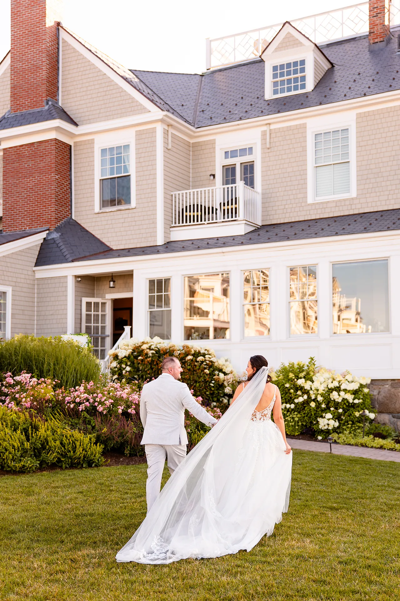 A bride and groom hold hands as they walk towards the Bar Harbor Inn and Spa during wedding portraits in Bar Harbor, Maine.