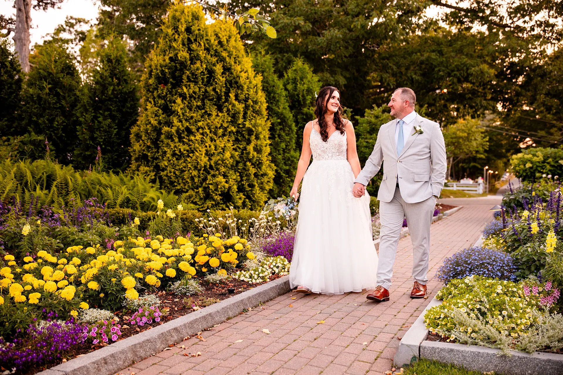 A bride and groom told hands as they walk through the garden at the Bar Harbor Inn and Spa during wedding portraits in Bar Harbor, Maine.