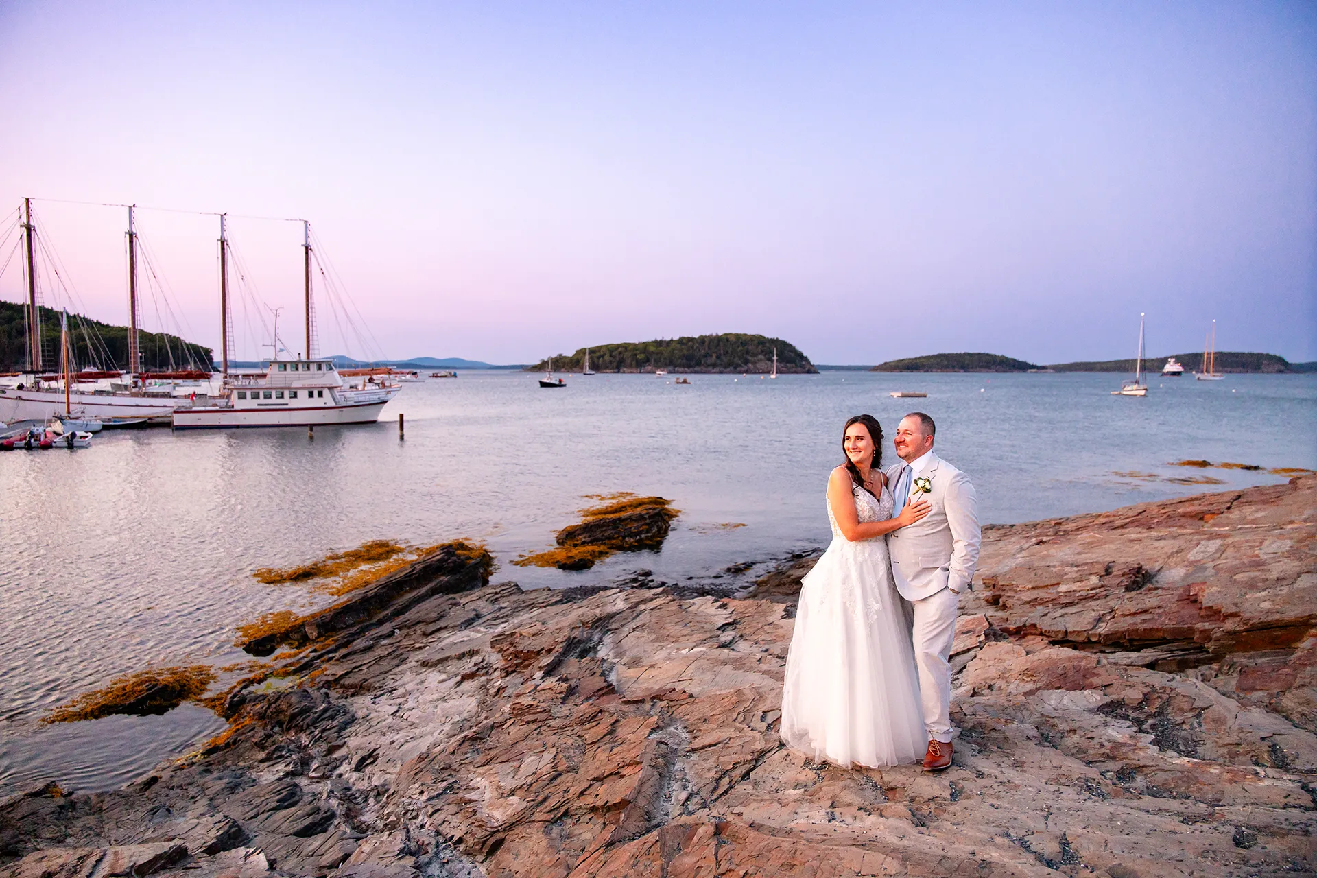 A bride and groom pose on a cliff over looking Frenchman Bay near the Bar Harbor Inn and Spa in Bar Harbor, Maine.
