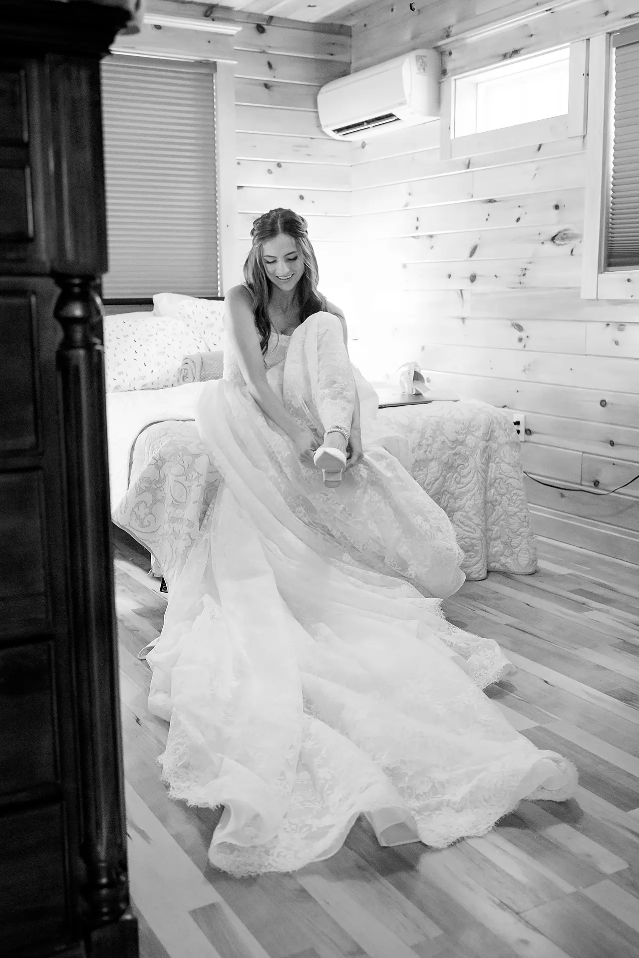 A bride smiles as she puts on her shoe as she gets for her wedding at the Kingsley Pines Camp In Raymond, Maine.