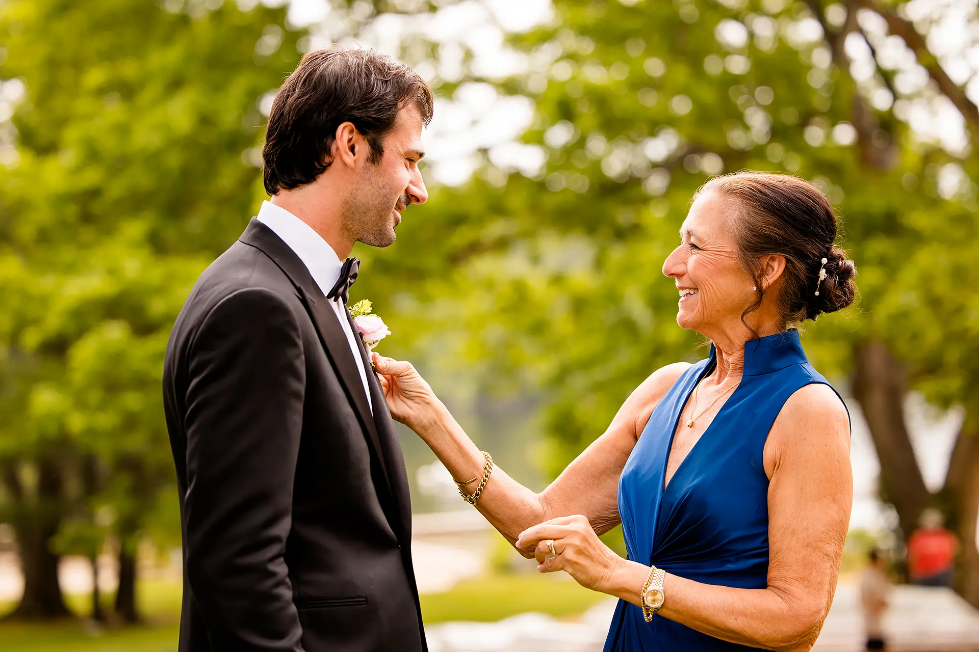 A mom helps a groom put on his boutonniere as he gets ready for his wedding at Kingsley Pines Camp in Raymond, Maine.