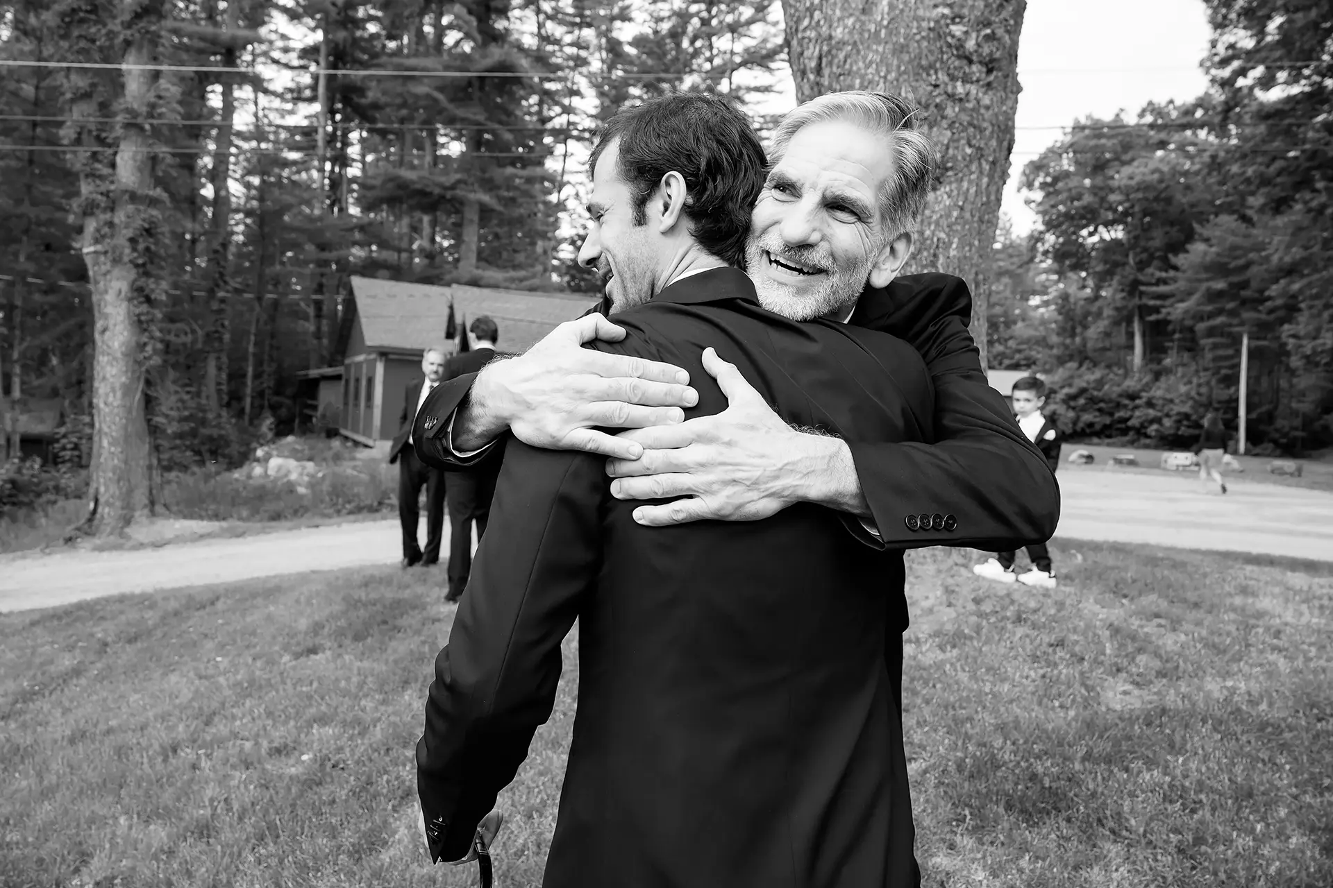A dad laughs as he hugs a groom as he gets ready for his wedding at Kingsley Pines Camp in Raymond, Maine.