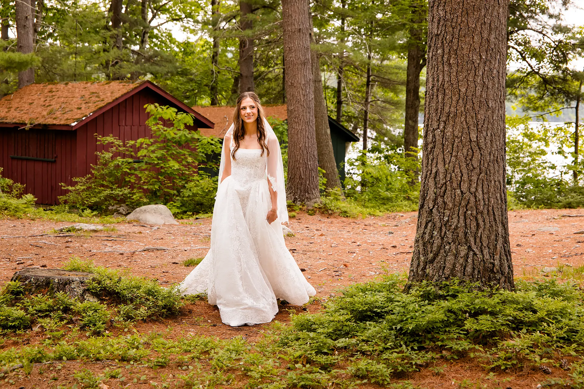 A bride smiles as she walks through pine needles at Kingsley Pines Camp in Raymond, Maine.