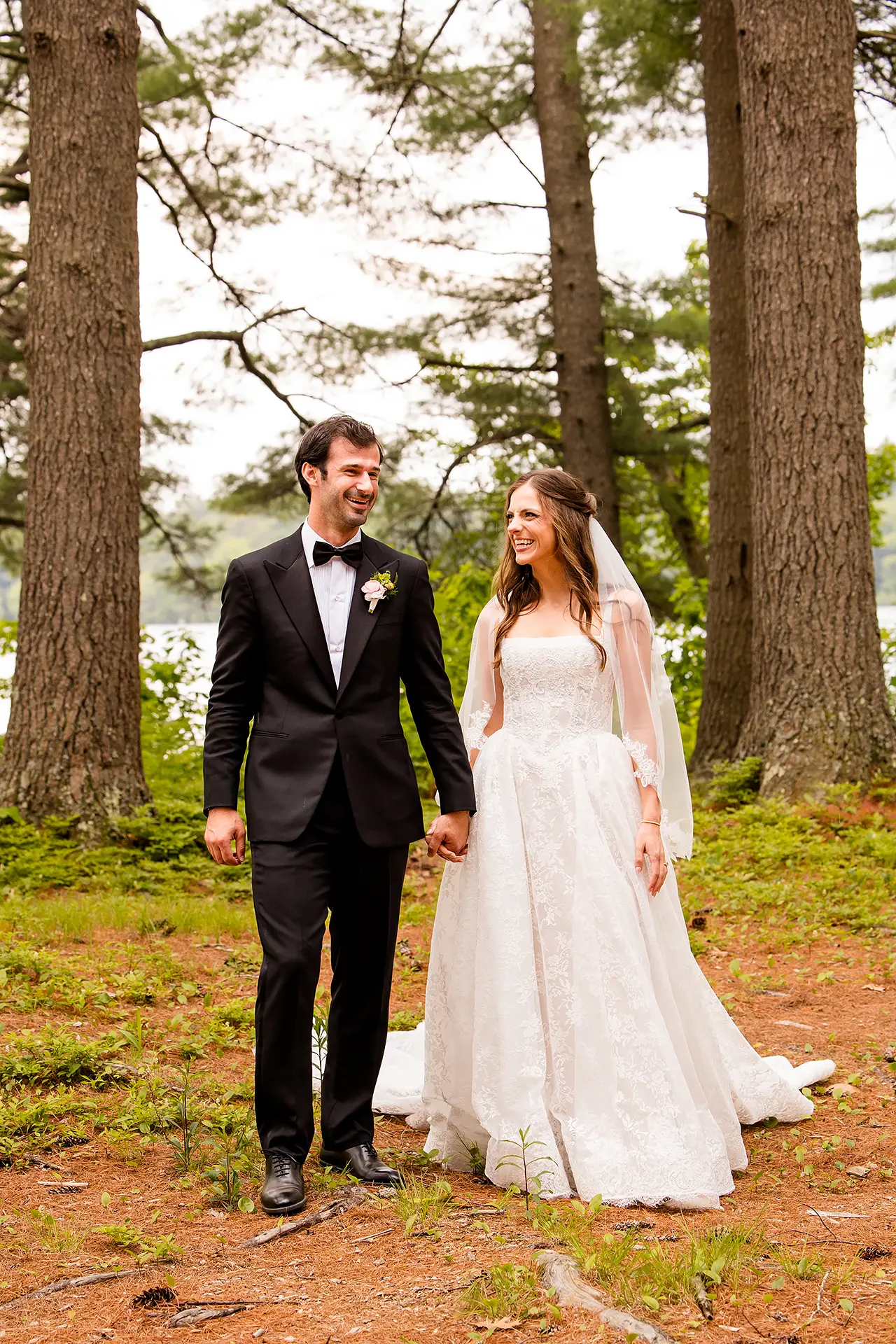A bride and groom hold hands and laugh during wedding portraits at Kingsley Pines Camp in Raymond, Maine.