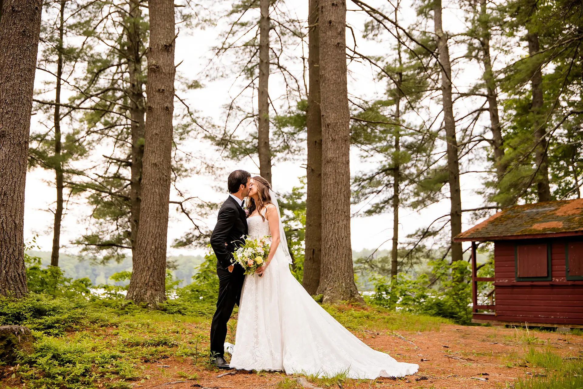 A bride and groom kiss during wedding portraits at Kingsley Pines Camp in Raymond, Maine.