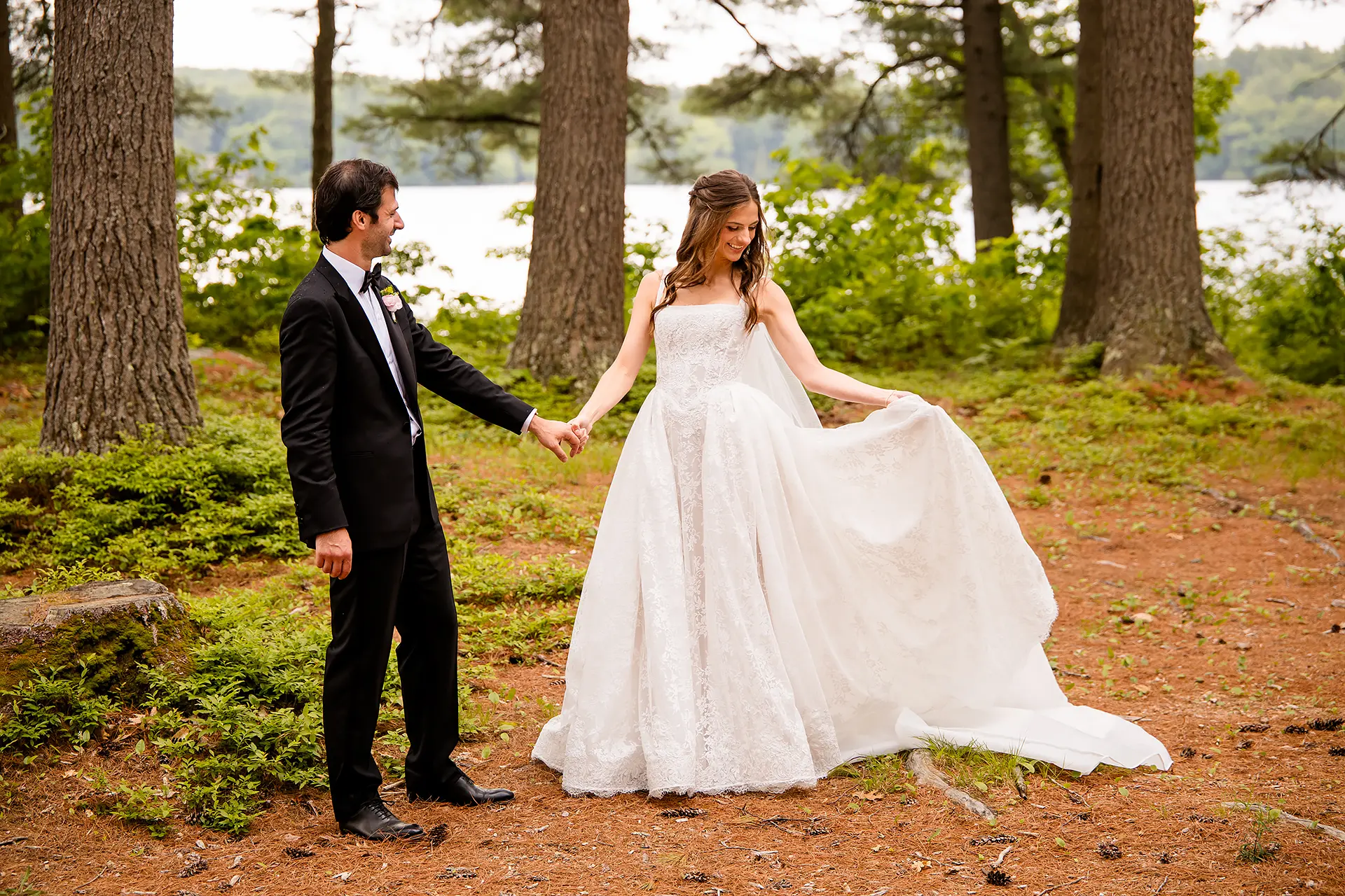 A bride and groom hold hands as a bride holds her dress during wedding portraits at Kingsley Pines Camp in Raymond, Maine.
