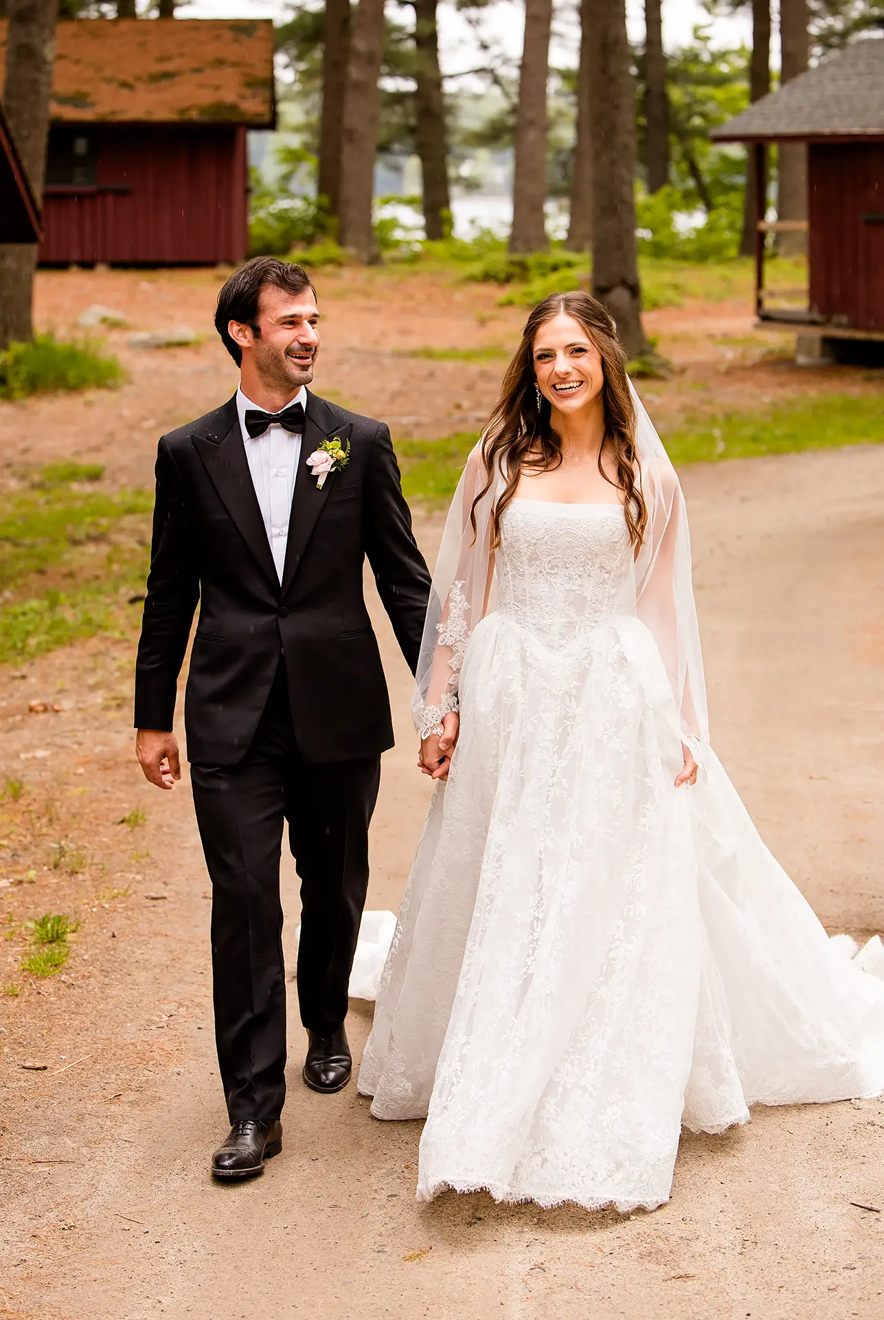 A bride and groom laugh as they hold hands and walk during wedding portraits at Kingsley Pines Camp in Raymond, Maine.