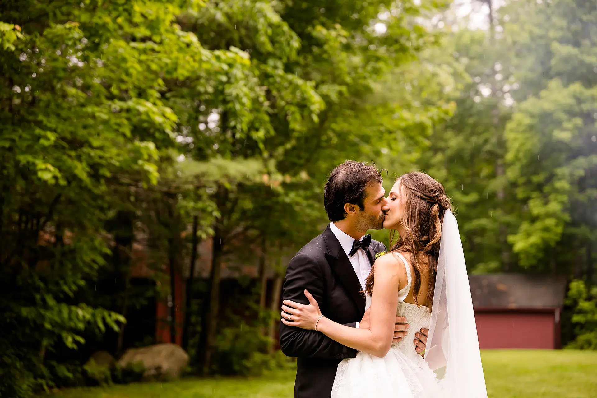 A bride and groom kiss as it rains during wedding portraits at Kingsley Pines Camp in Raymond, Maine.