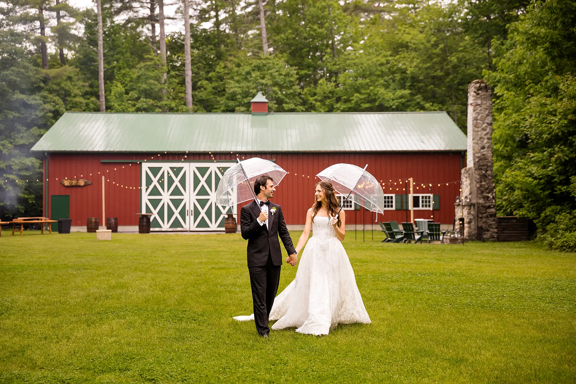 A bride and groom hold umbrellas and walk together during wedding portraits at Kingsley Pines Camp in Raymond, Maine.