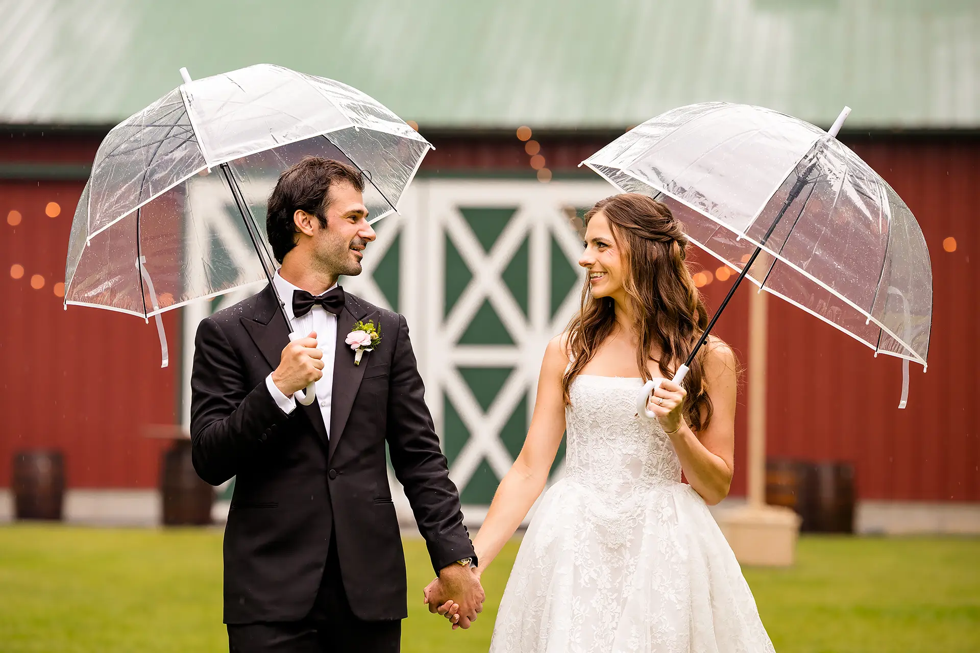 A bride and groom hold umbrellas and smile at each other during wedding portraits at Kingsley Pines Camp in Raymond, Maine.