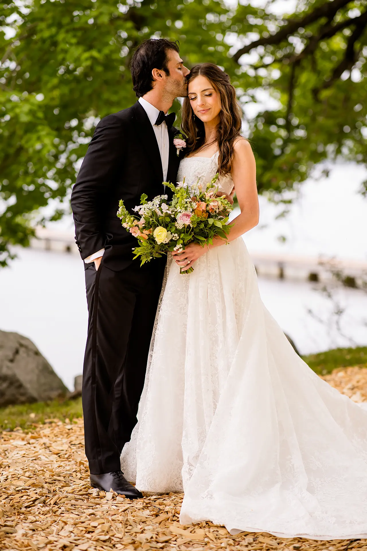 A groom kisses a bride on the head as she smiles during wedding portraits at Kingsley Pines Camp in Raymond, Maine.