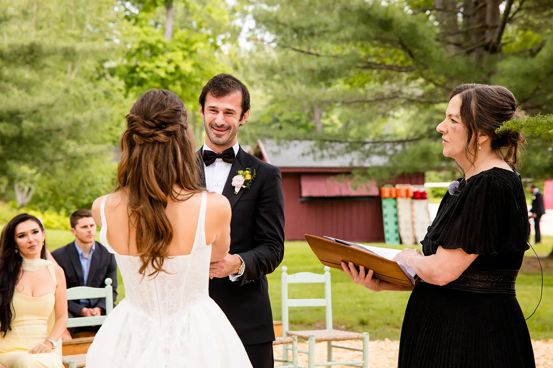 A groom smiles as he holds a bride's hands during a wedding ceremony at Kingsley Pines Camp in Raymond, Maine.