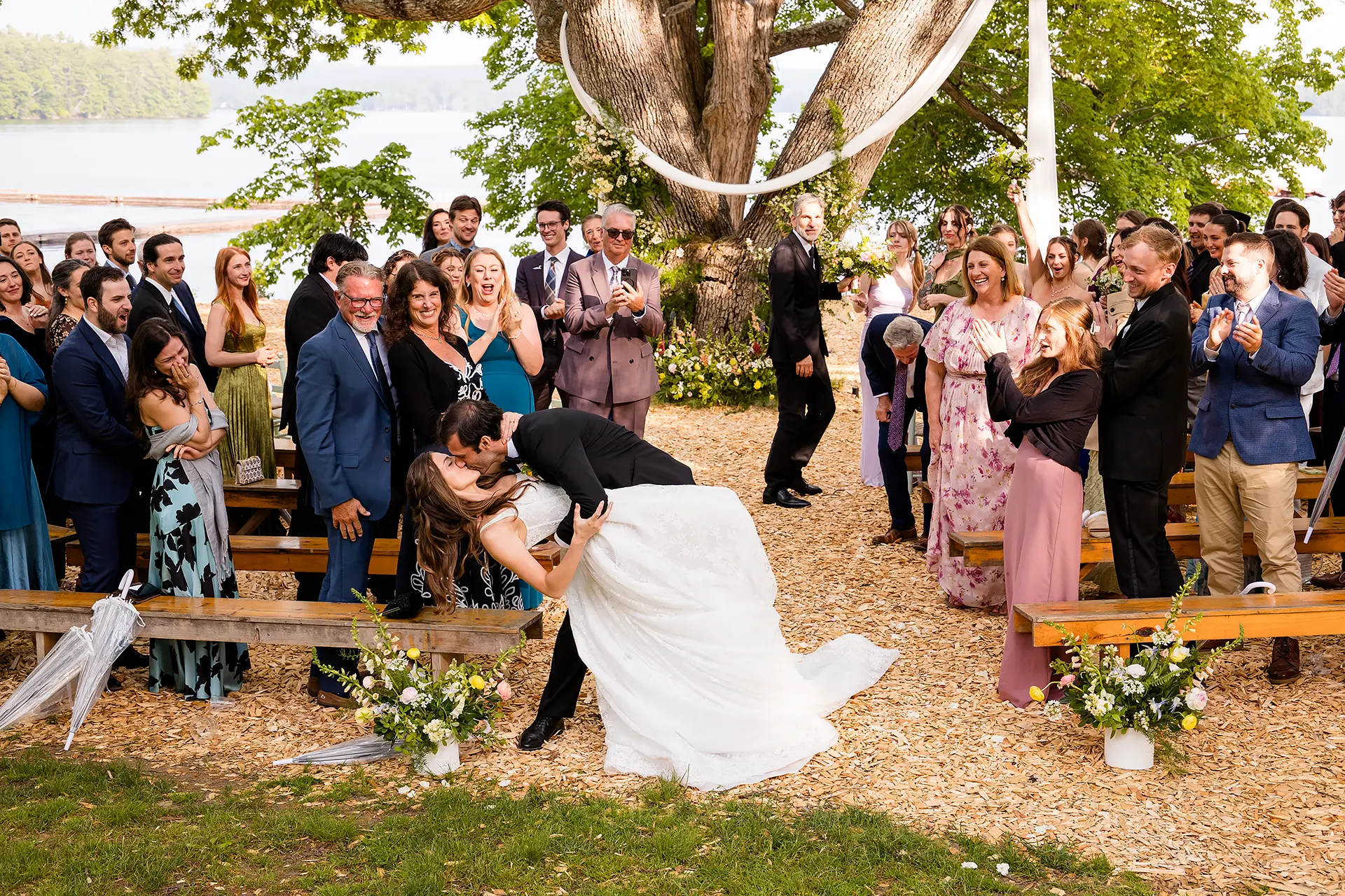 A groom dips a bride as they kiss while guests cheer during a wedding ceremony at Kingsley Pines Camp in Raymond, Maine.