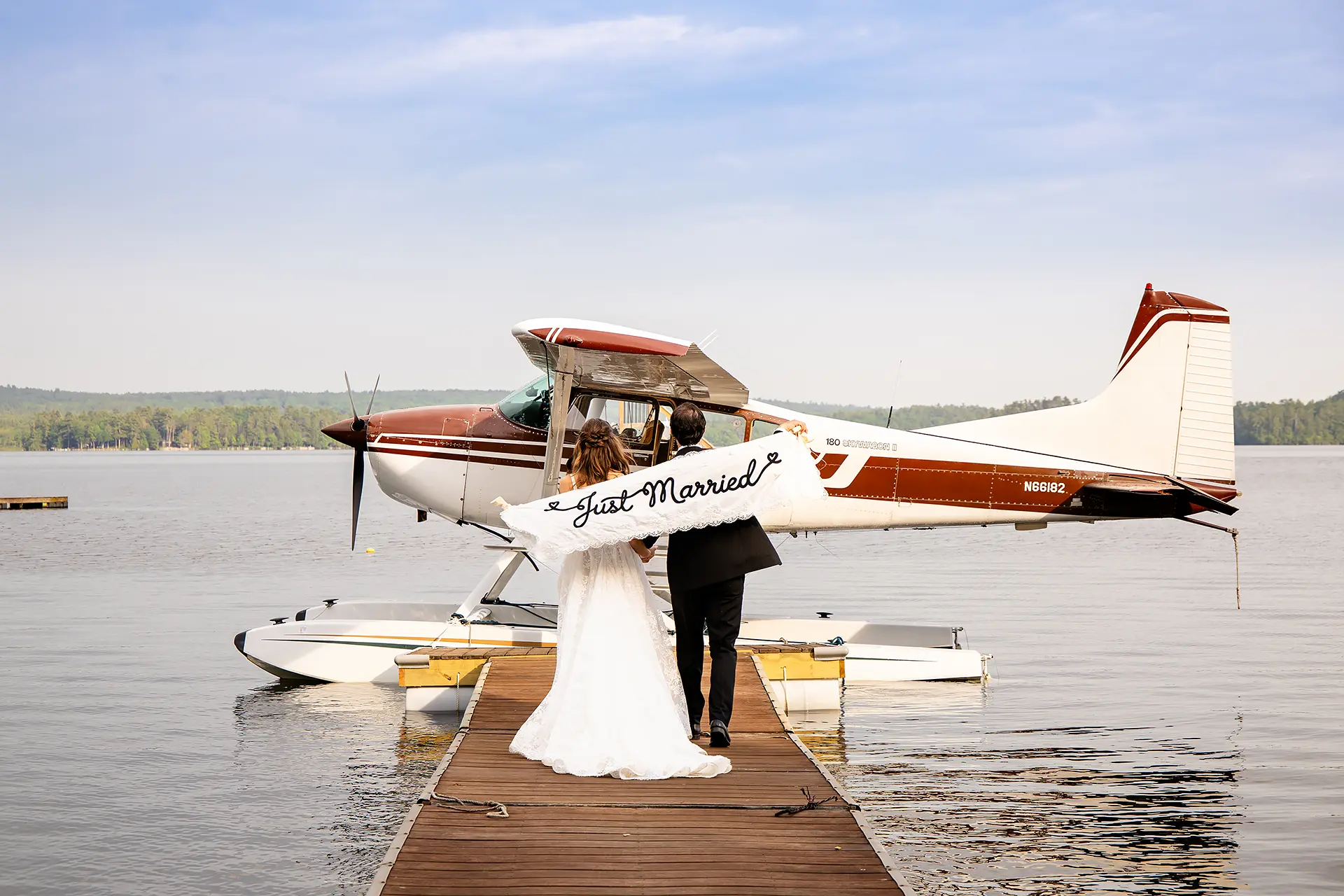 A newly married couple hold a just married sign as they walk towards a lake plane at Kingsley Pines Camp in Raymond, Maine.