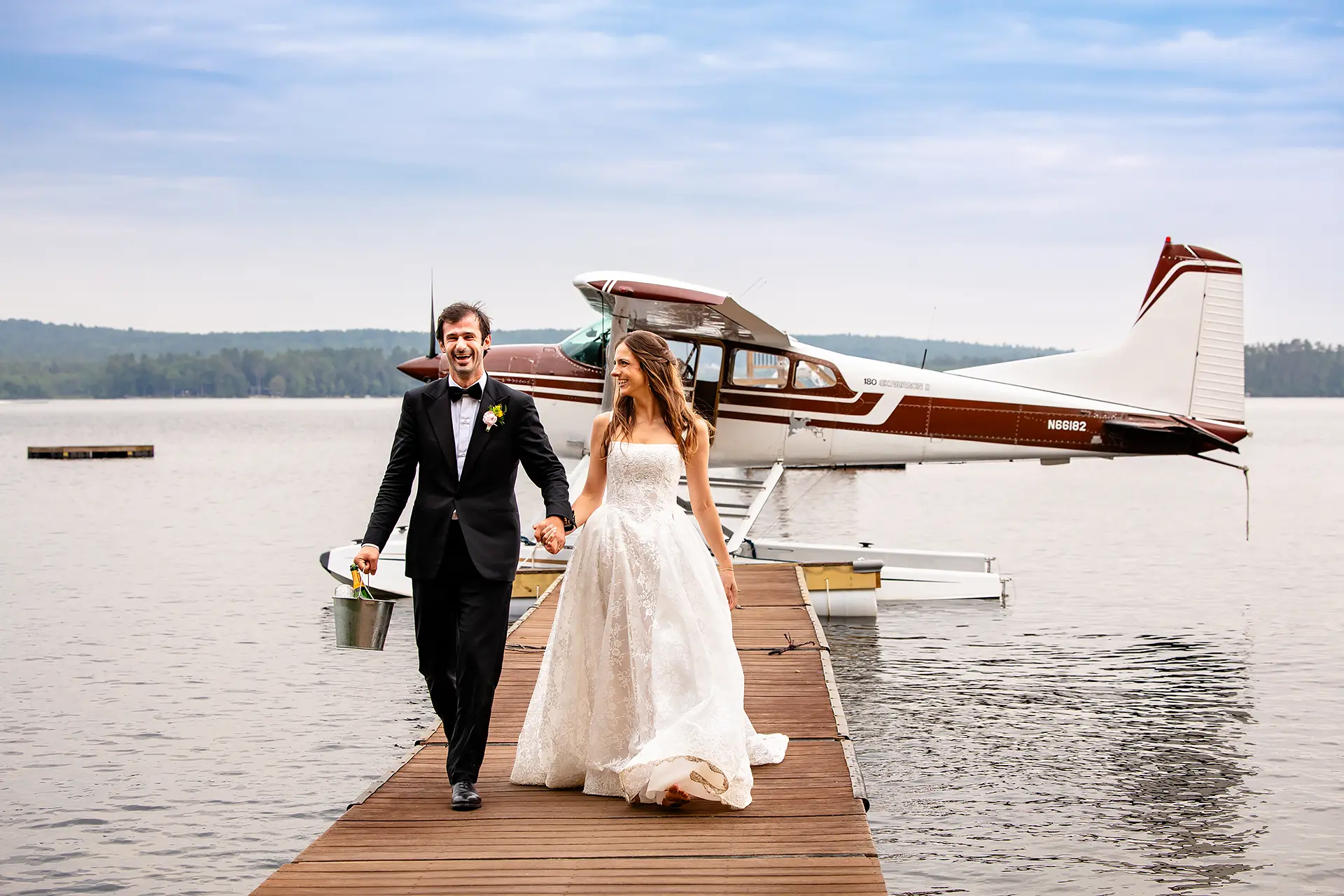 A newly married couple hold hands as they walk along a dock with a lake plane behind them at Kingsley Pines Camp in Raymond, Maine.