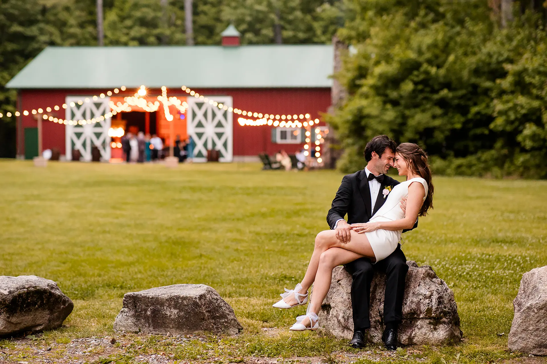 A bride sits on a groom's lap as they smile and rest their heads together during a wedding reception at Kingsley Pines Camp in Raymond, Maine.