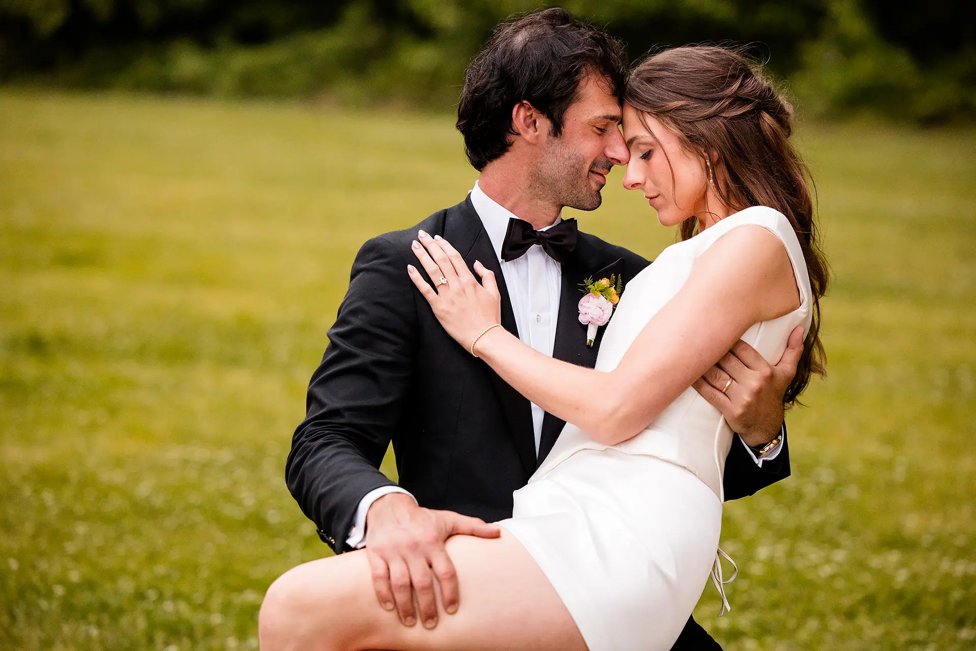 A bride sits in a groom's lap as they rest their heads together during wedding portraits at Kingsley Pines Camp in Raymond, Maine.