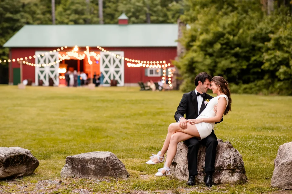 A bride sits on a groom's lap as they smile and rest their heads together during a wedding reception at Kingsley Pines Camp in Raymond, Maine.