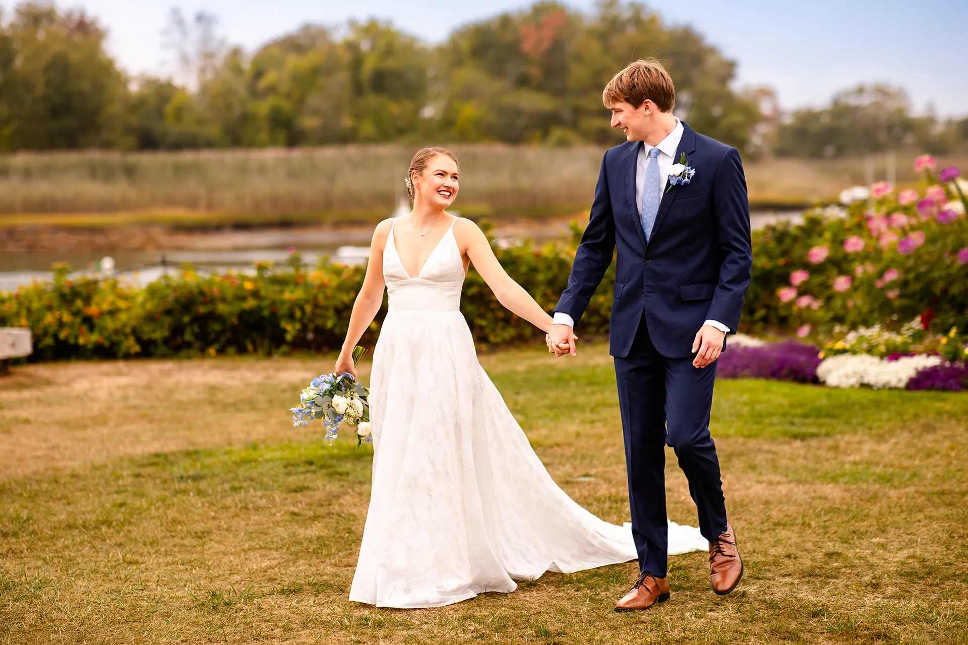 A bride and groom hold hands and walk during wedding portraits at the Nonantum Resort in Kennebunkport, Maine.