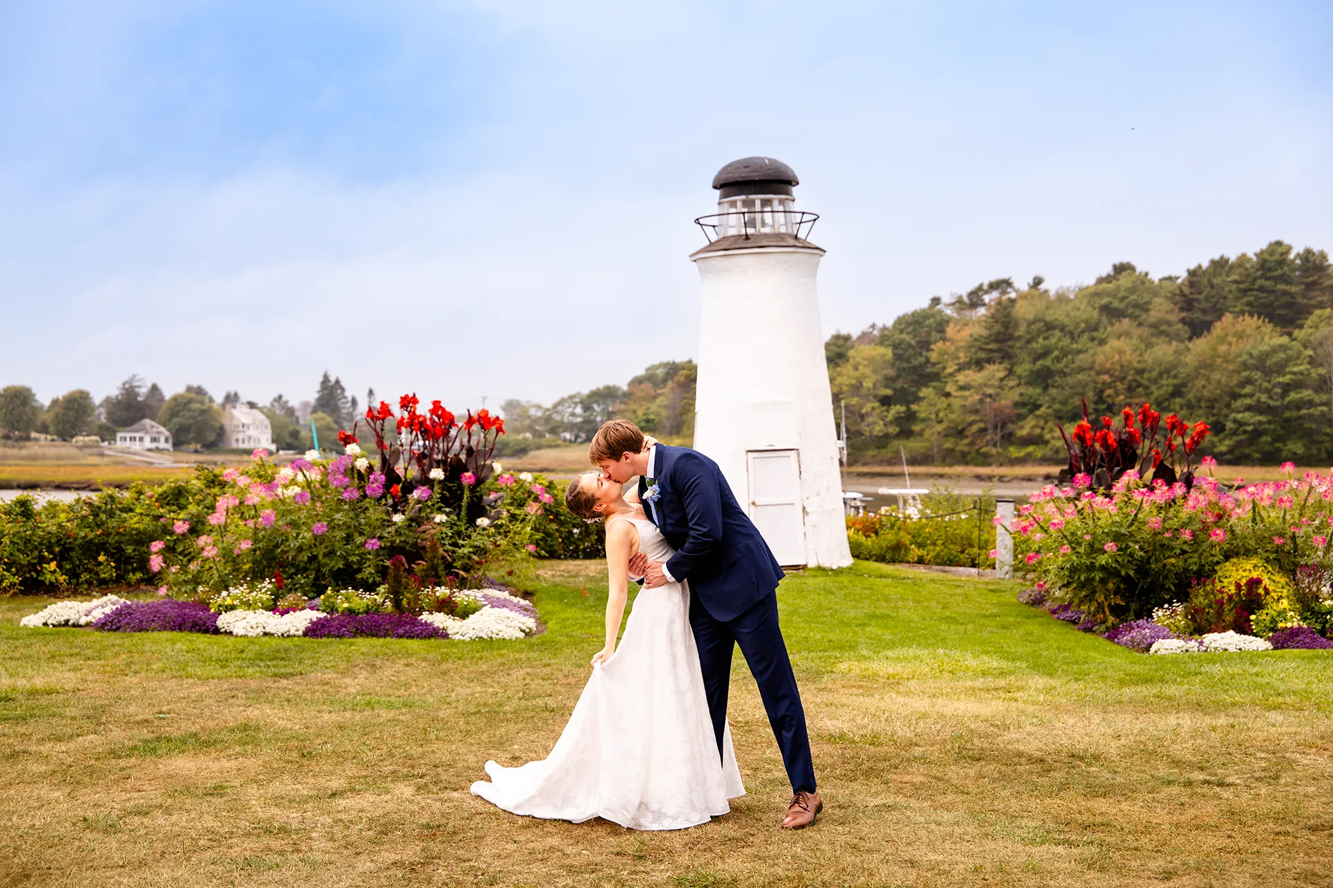 A bride and groom kiss in front of a lighthouse during wedding portraits at the Nonantum Resort in Kennebunkport, Maine.