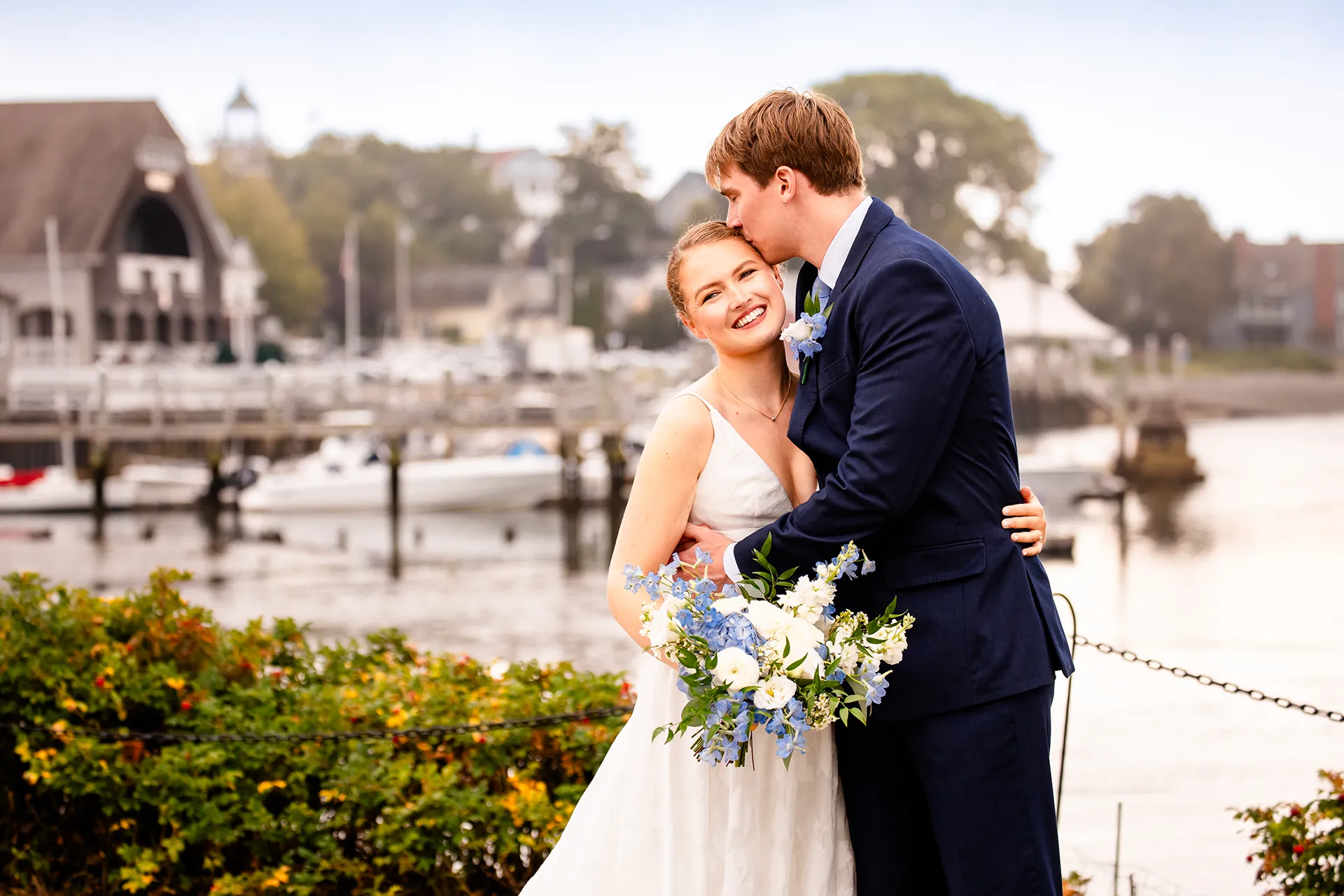 A groom kisses a smiling bride on the head during wedding portraits at the Nonantum Resort in Kennebunkport, Maine.